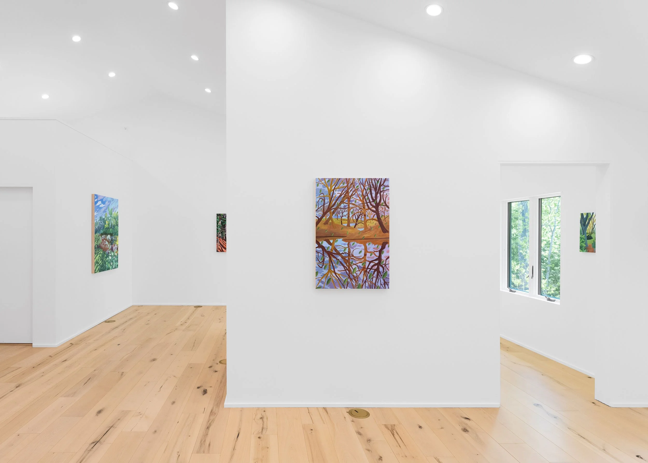 Art gallery with white walls displaying colorful paintings, wooden floor, and a window showing greenery outside.