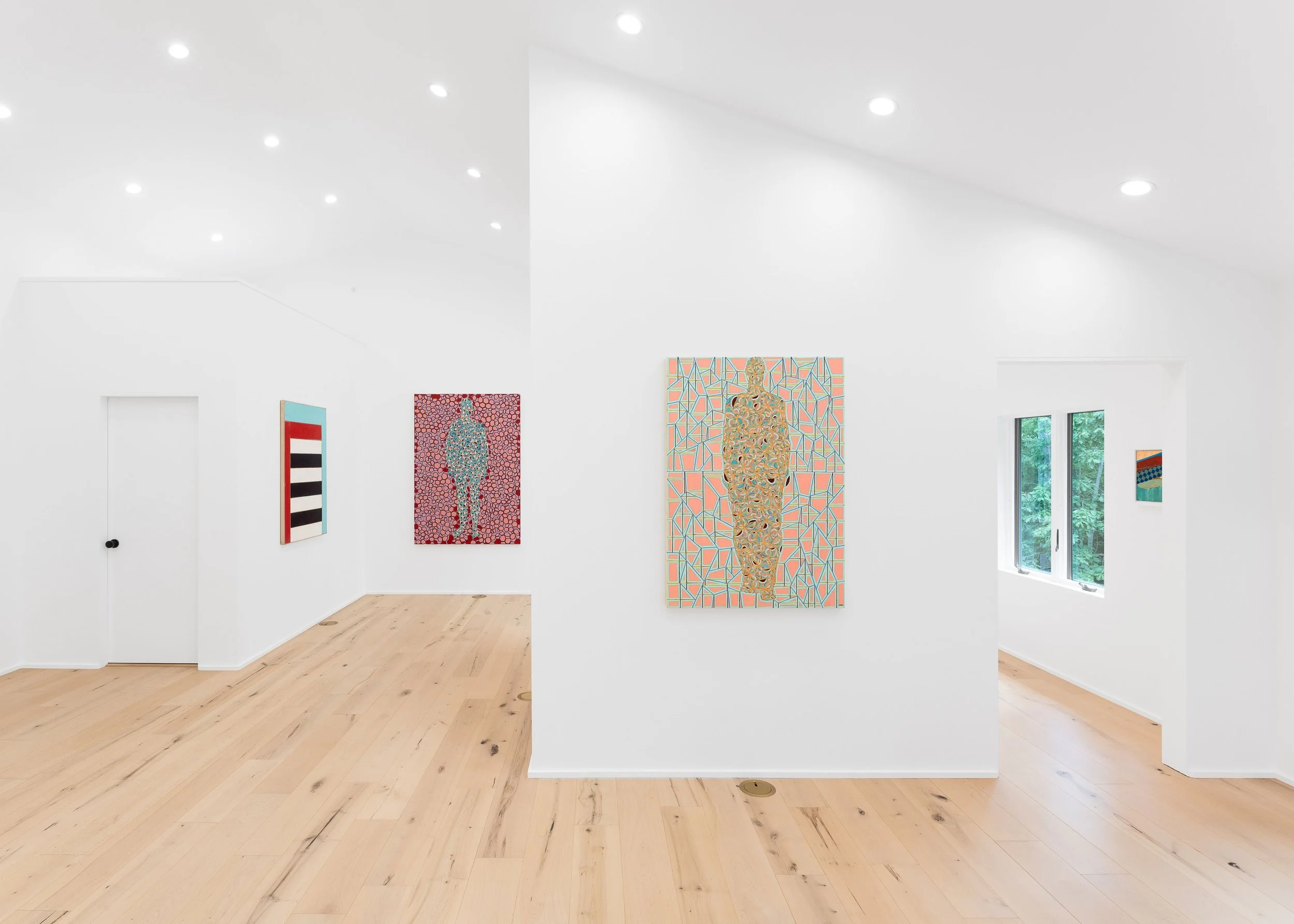 An art gallery with white walls and several colorful paintings on display, natural light streaming in through large windows, and a light wooden floor.