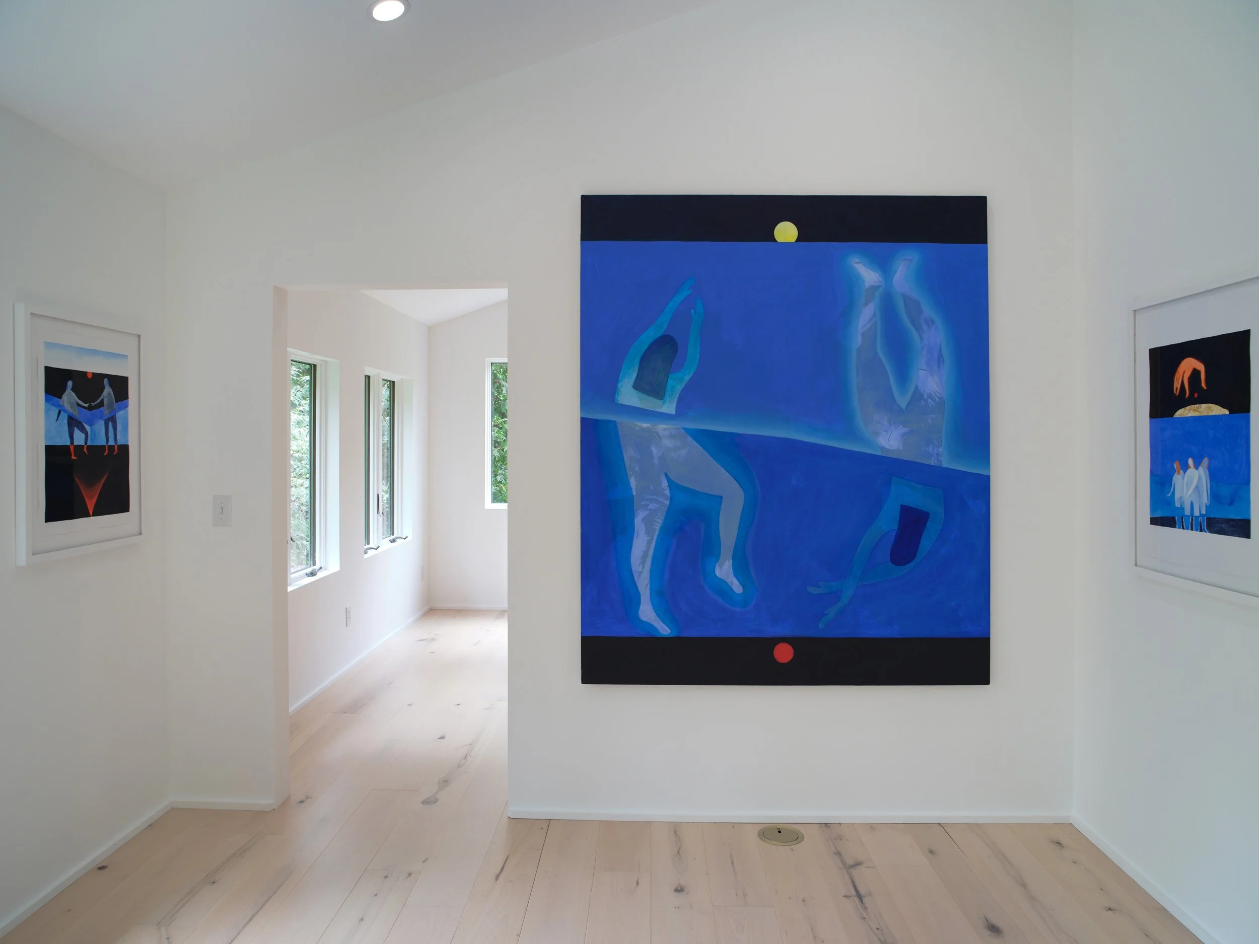Contemporary art gallery with white walls displaying several colorful abstract paintings of human figures and figures with rounded shapes, in bright colors such as blue and black. Large windows allow natural light into the space.