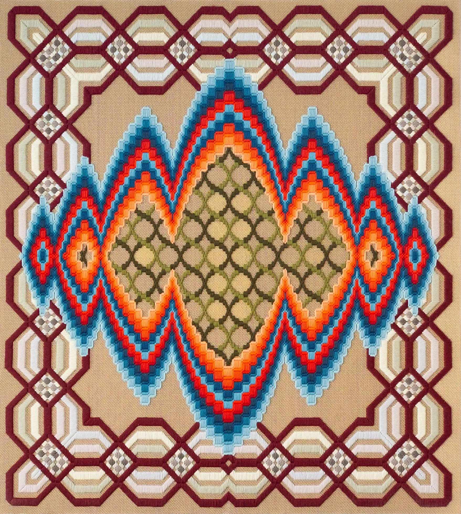 A colorful, geometric-patterned textile with intricate cross-stitching in shades of red, blue, orange, green, white, and beige, forming a symmetrical design with mountains, diamonds, and other shapes.