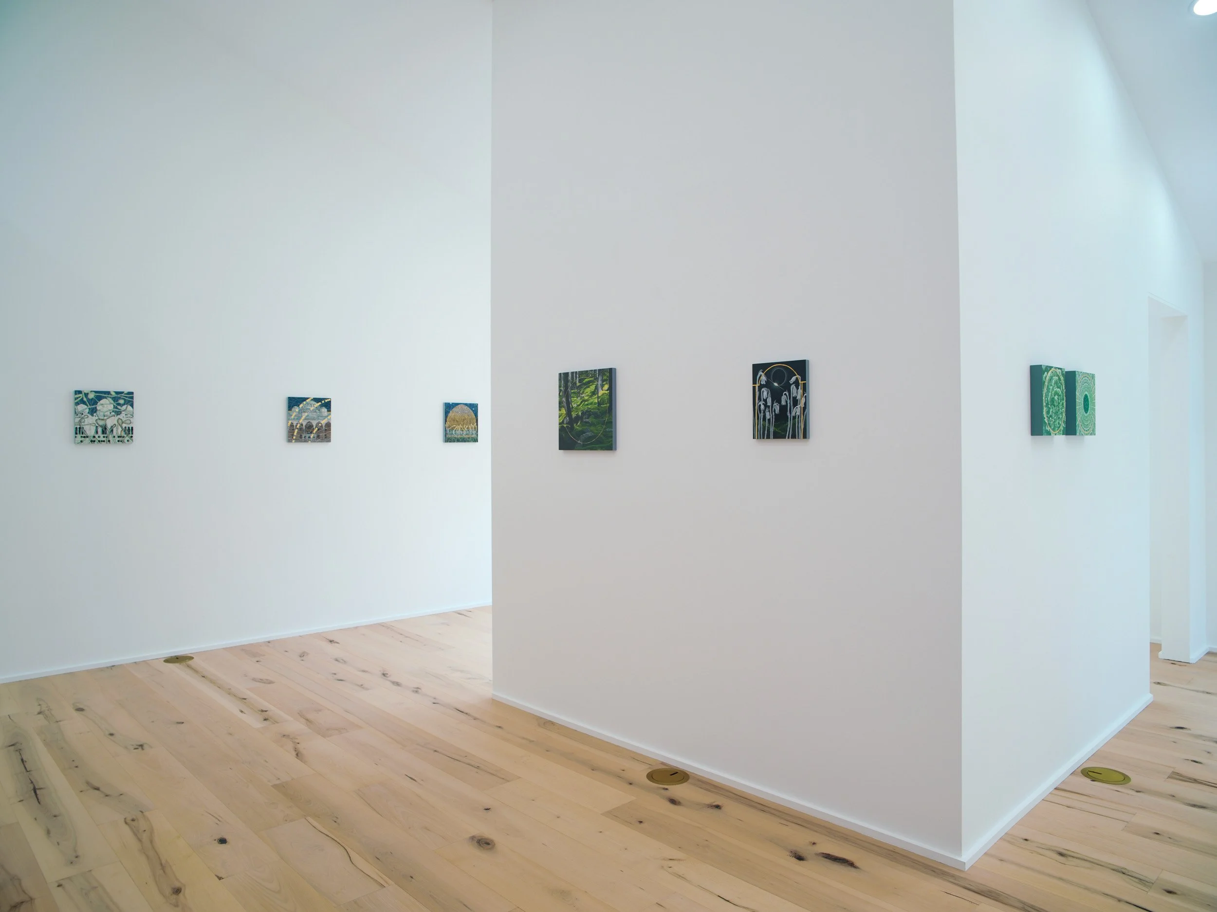 Gallery wall with small paintings on white walls in a room with light wood flooring.