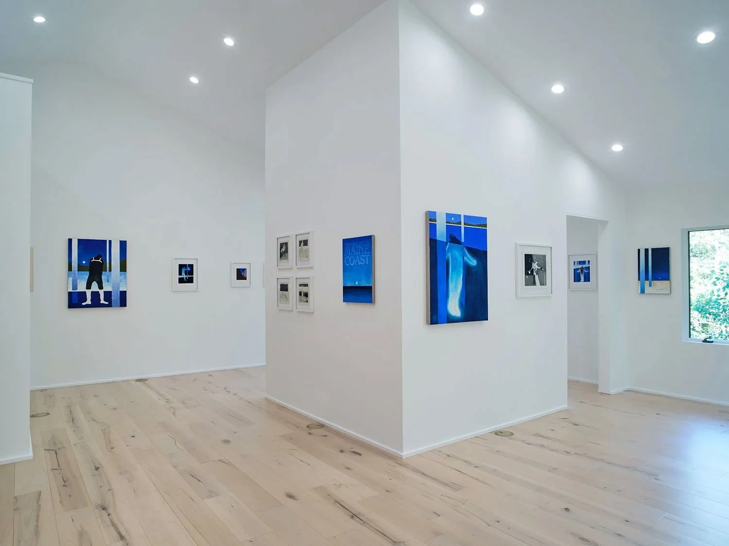 Art gallery with white walls, light wood floor, and blue-toned artwork displayed.