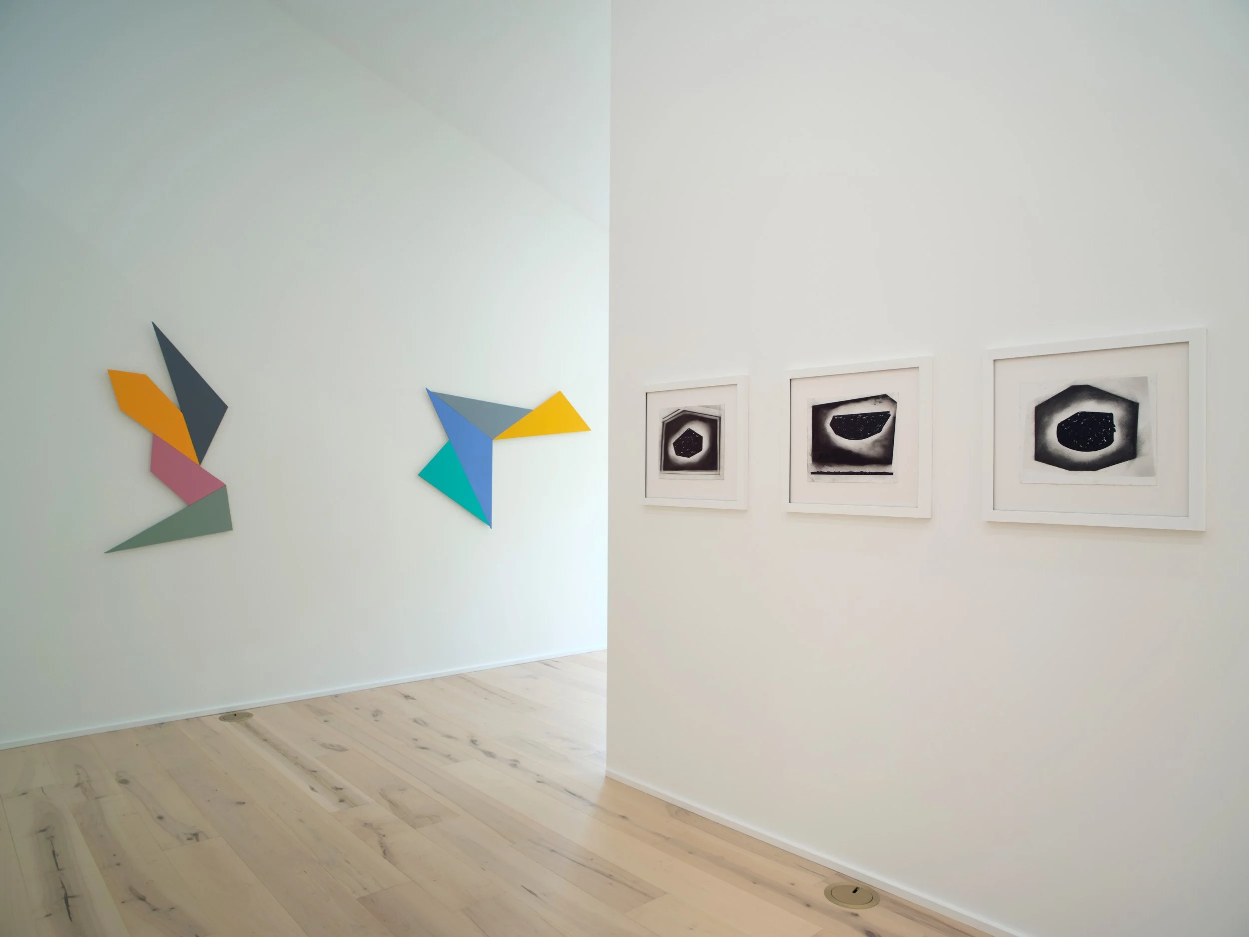 Art gallery wall with colored abstract geometric shapes on the left and a series of black and white cosmic or planetary images framed on the right side.