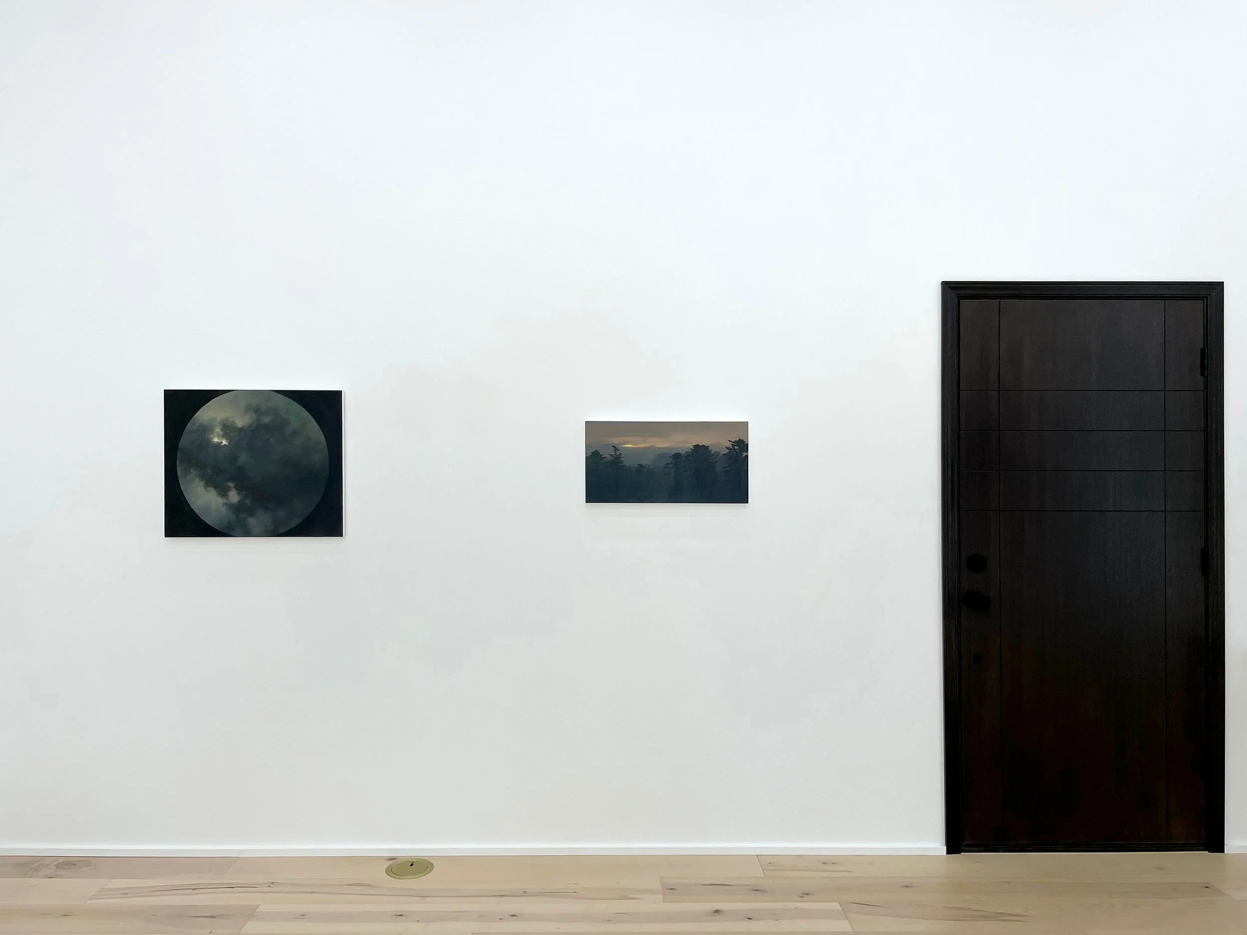 Minimalist gallery wall with three landscape photographs and a large black door on a white gallery wall.
