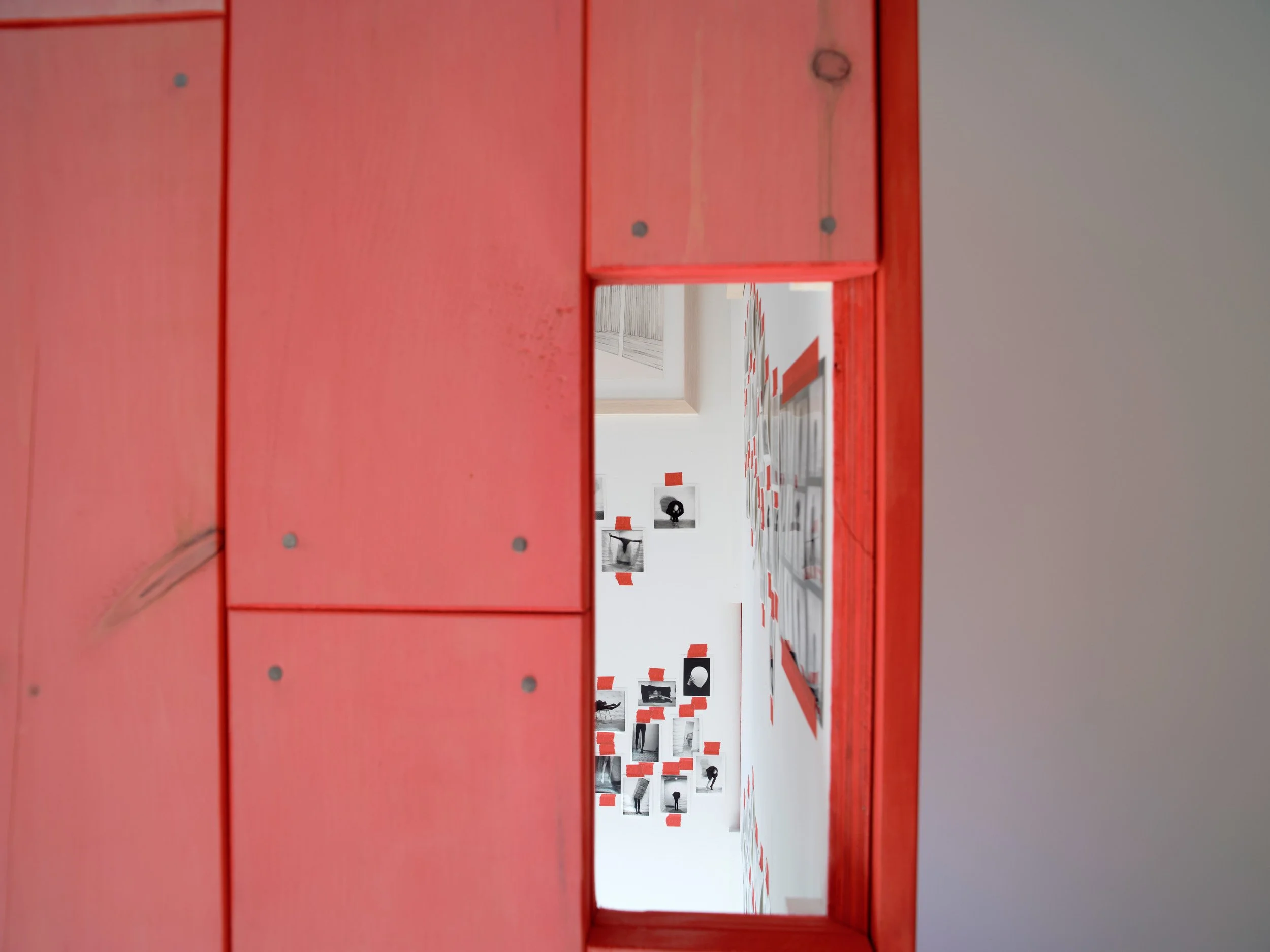 View through a rectangular opening in a red wall into an art gallery with black and white photographs and red and white wall decoration.