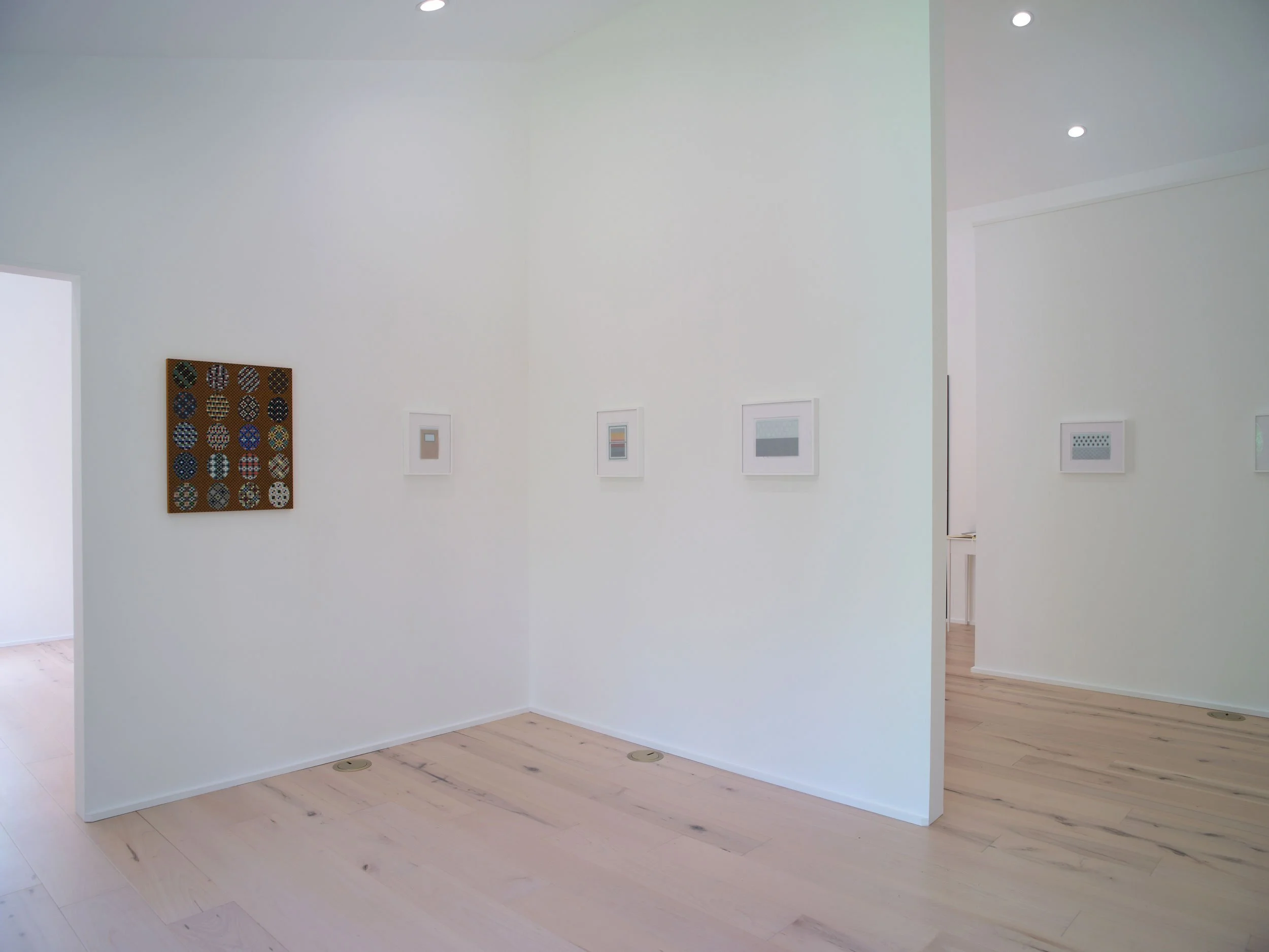 Interior of a modern art gallery with white walls, wooden floors, and framed artwork. Recessed ceiling lights illuminate the space.
