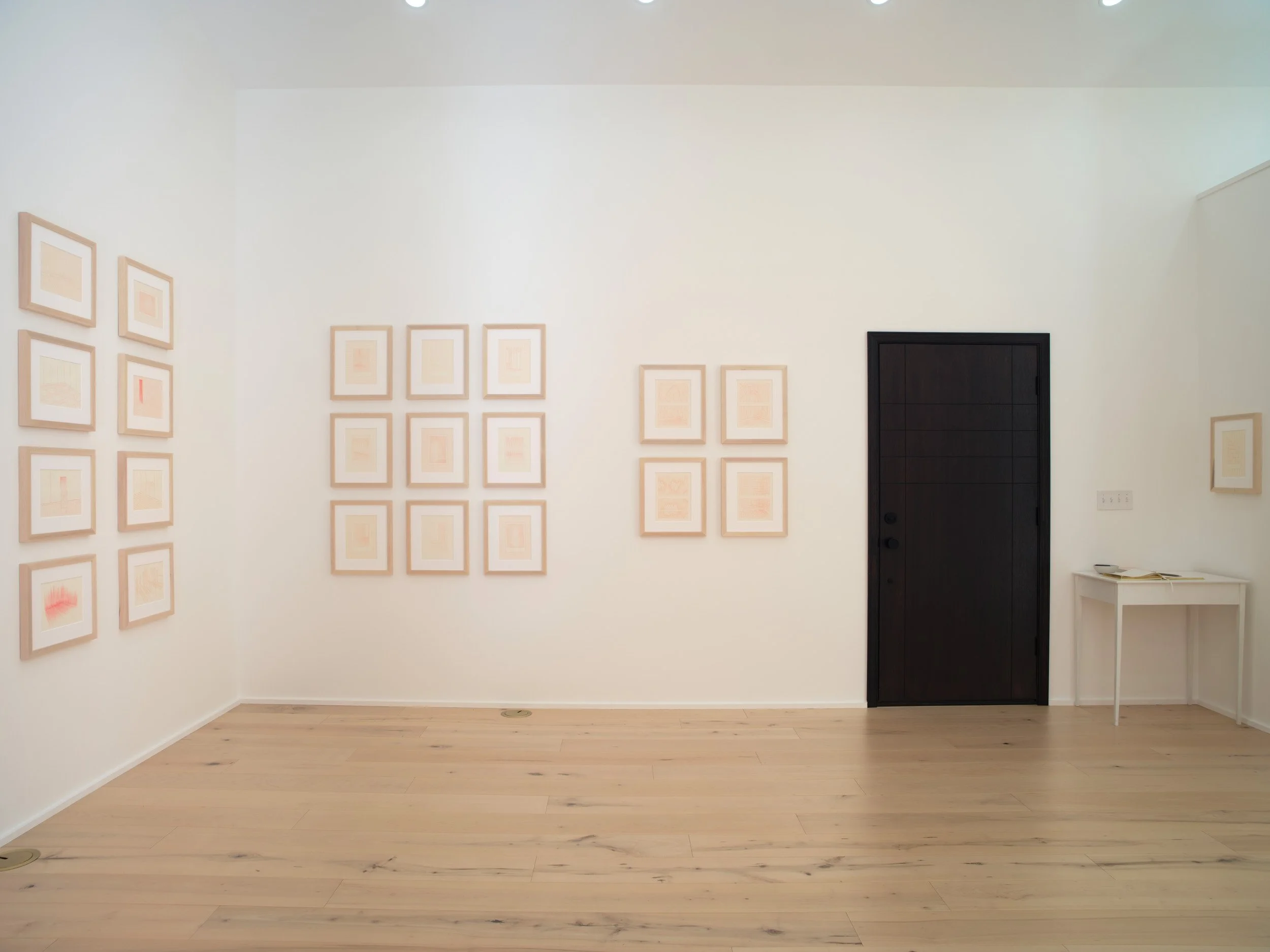 An art gallery wall featuring multiple framed pieces of artwork, with a black door on the right side and a white table beside it.