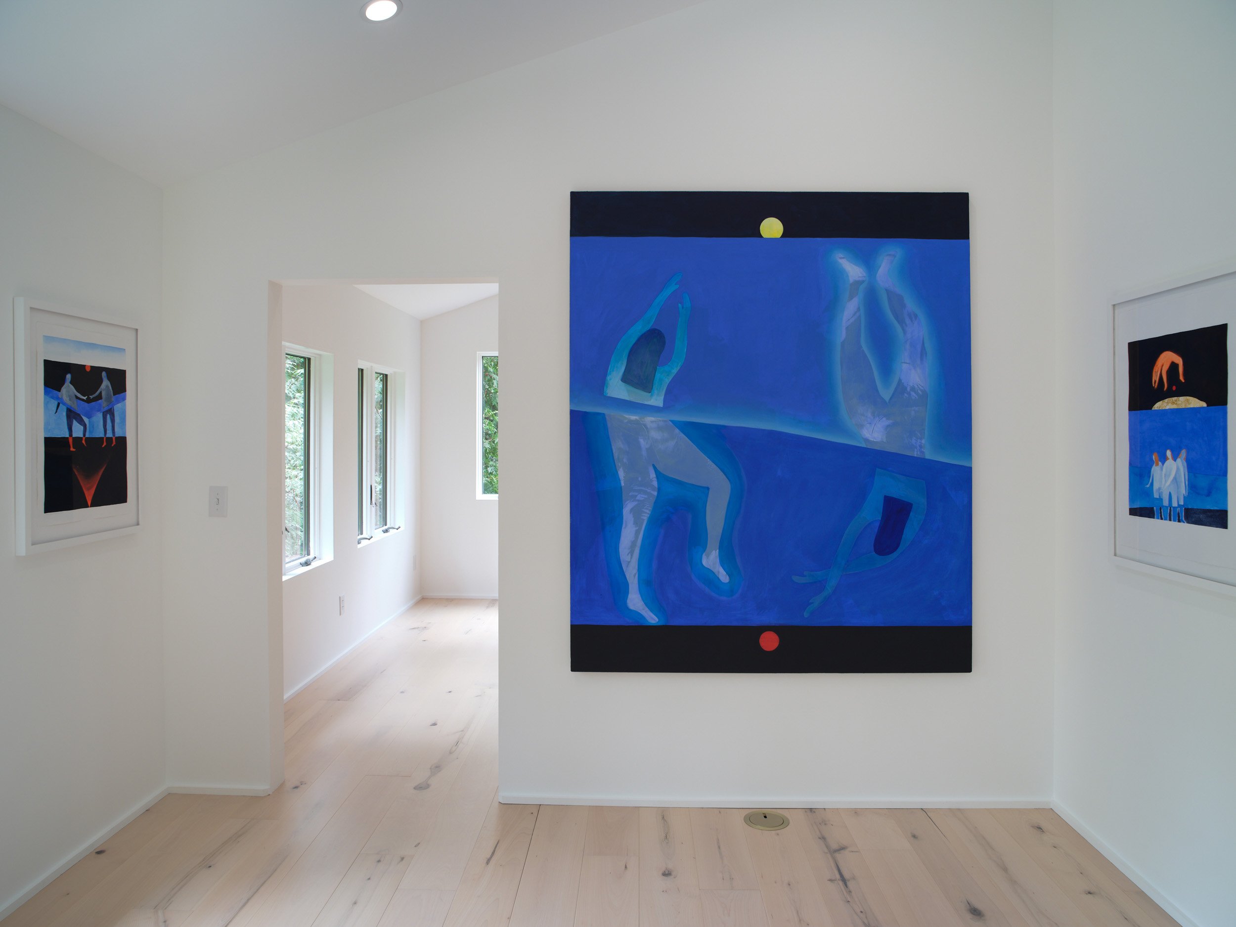 Art gallery display with large blue paintings of abstract human figures on white walls, natural light coming through windows.