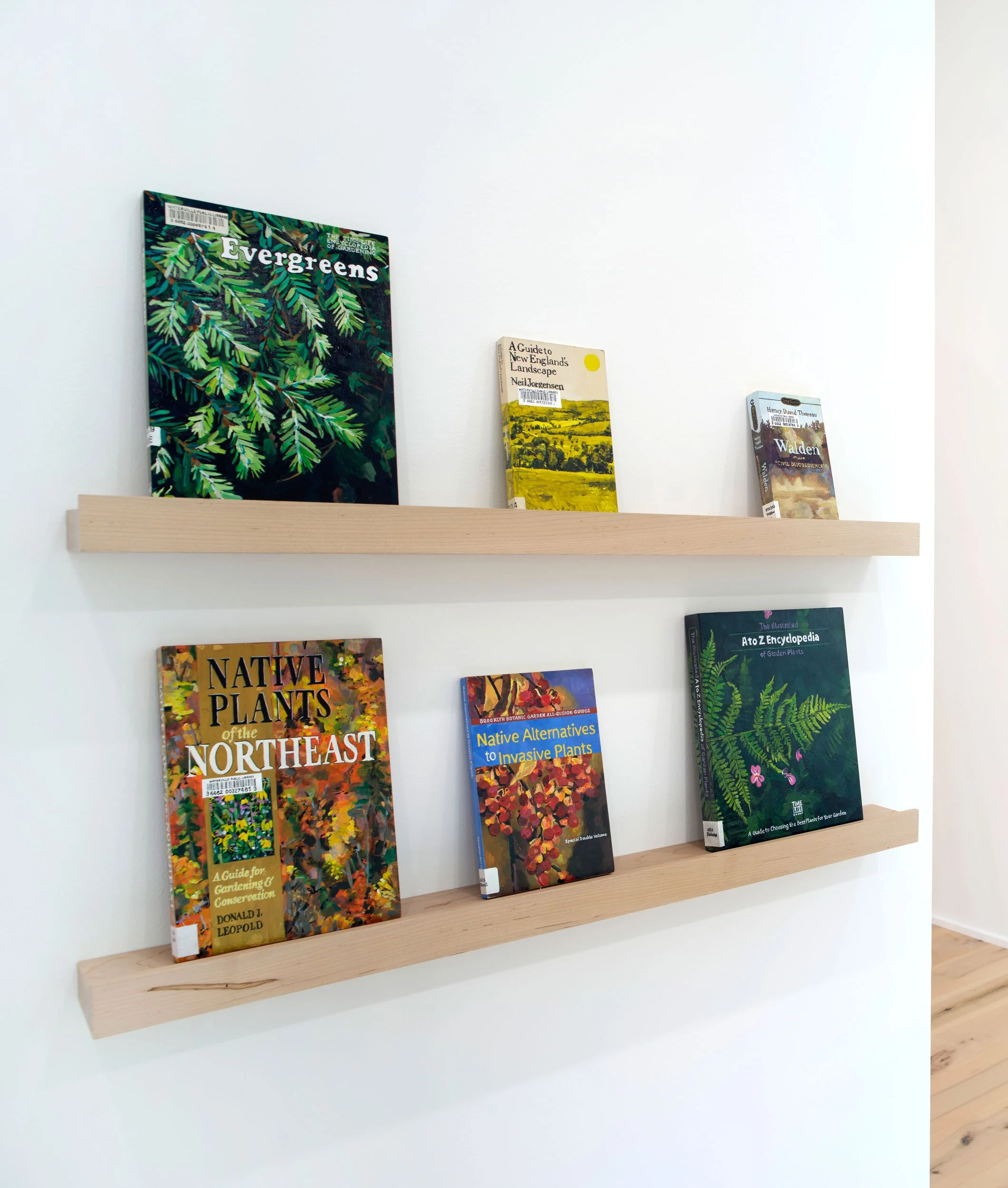 Books on gardening displayed on a wooden shelf against a white wall.