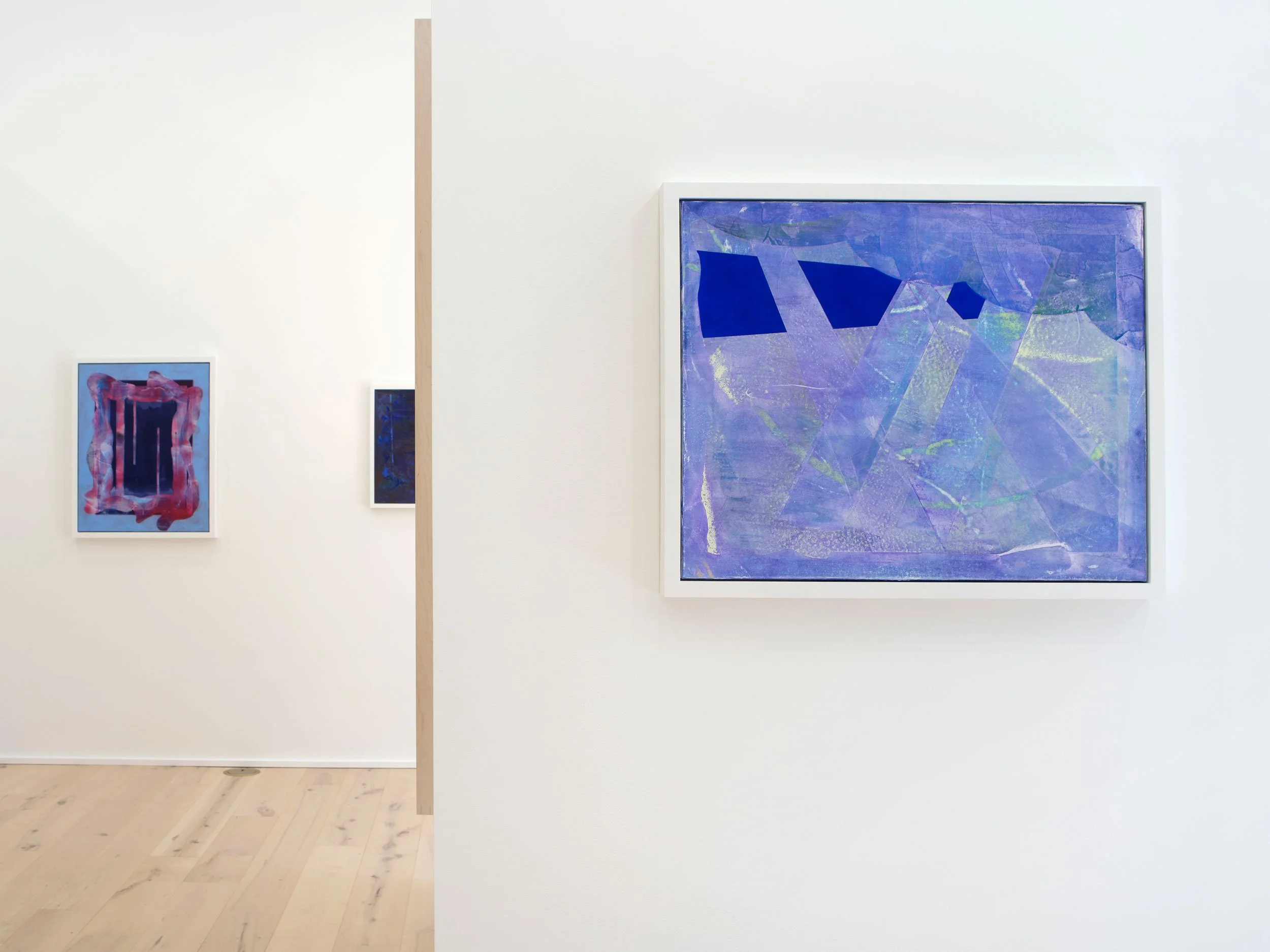 Art gallery with abstract paintings, including a large blue and purple piece on the right and smaller colorful works on the left.