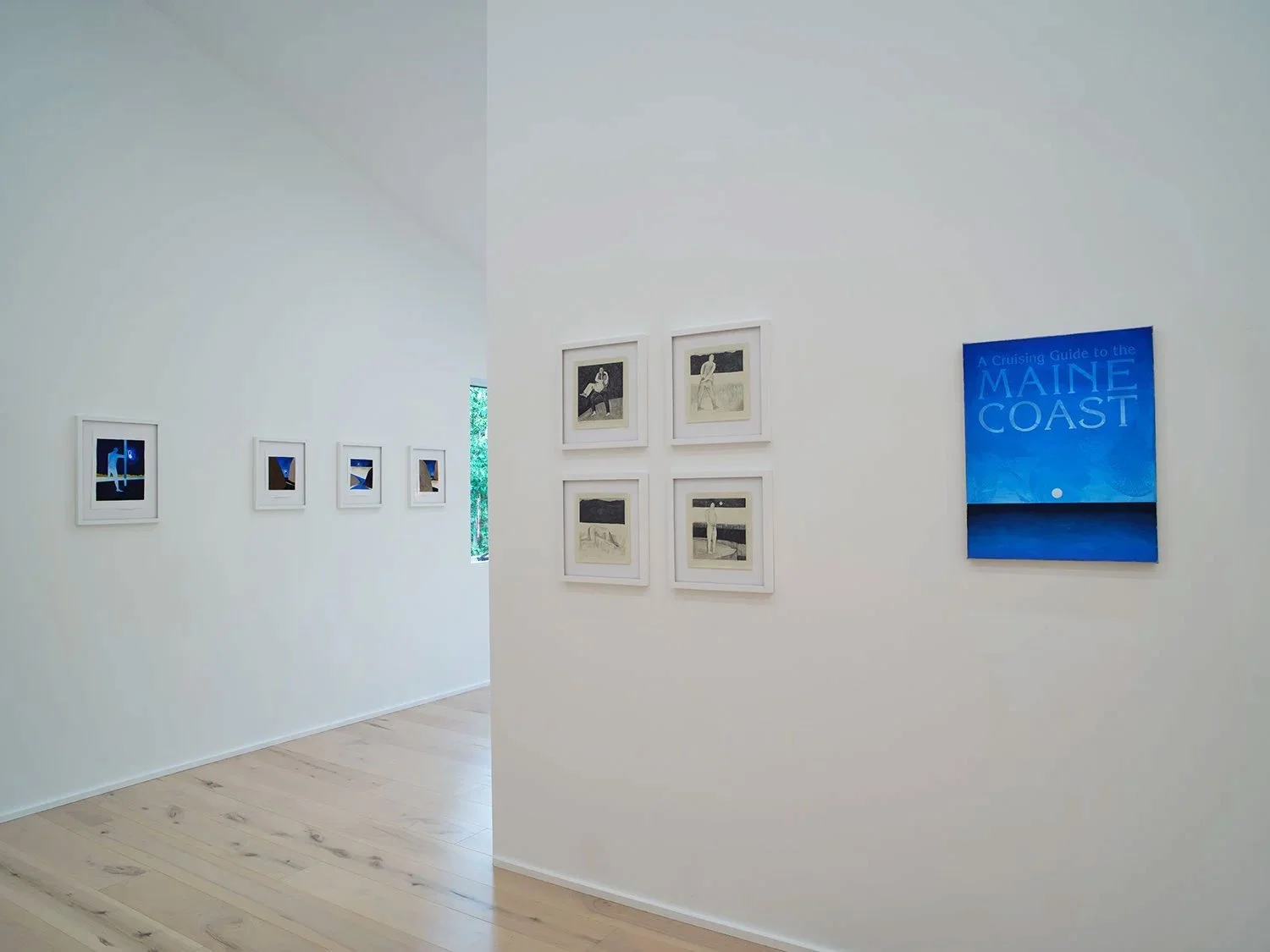 Art gallery with framed photographs and illustrations on white walls, including a blue poster on the right that reads "A Cruising Guide to the Maine Coast".