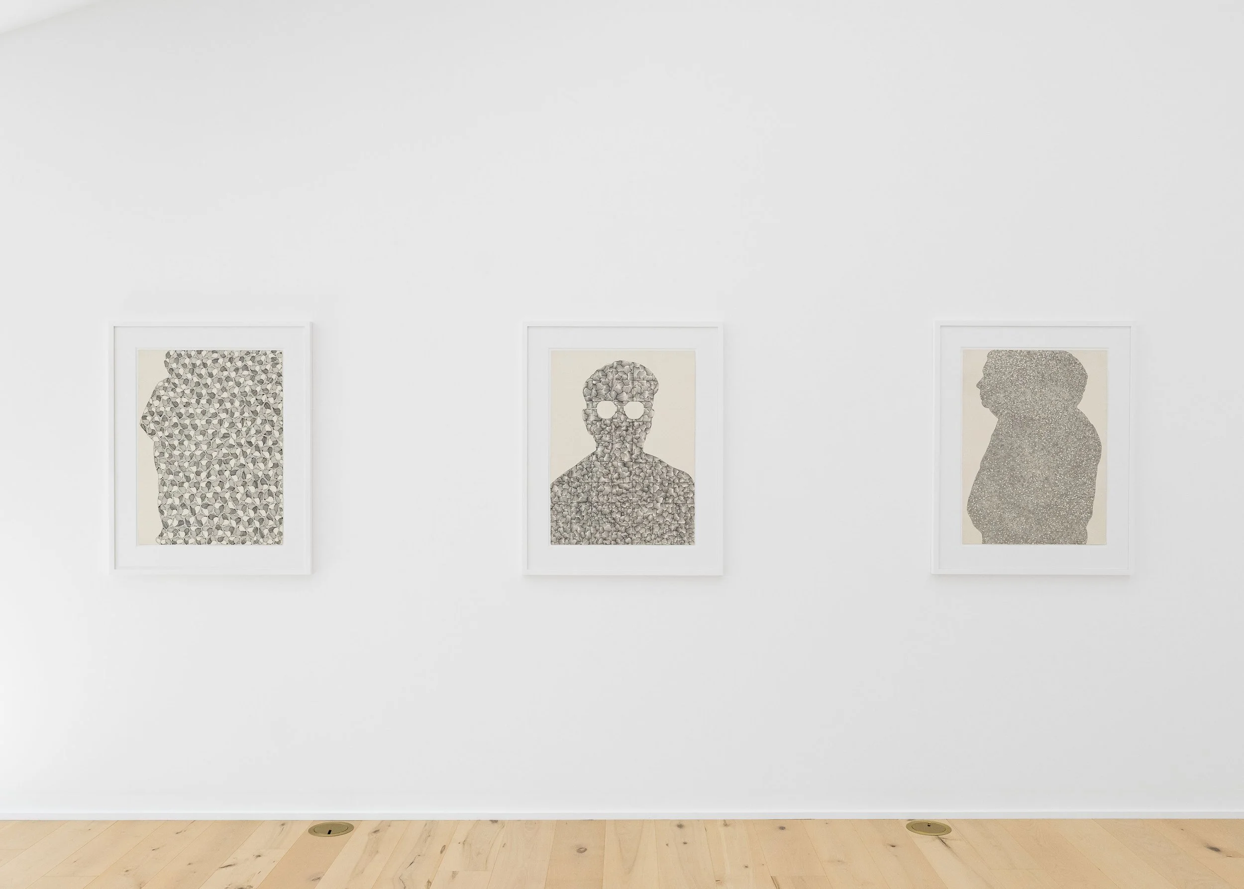Three framed drawings on a white gallery wall feature abstract silhouettes and portrait designs in shades of gray and black.