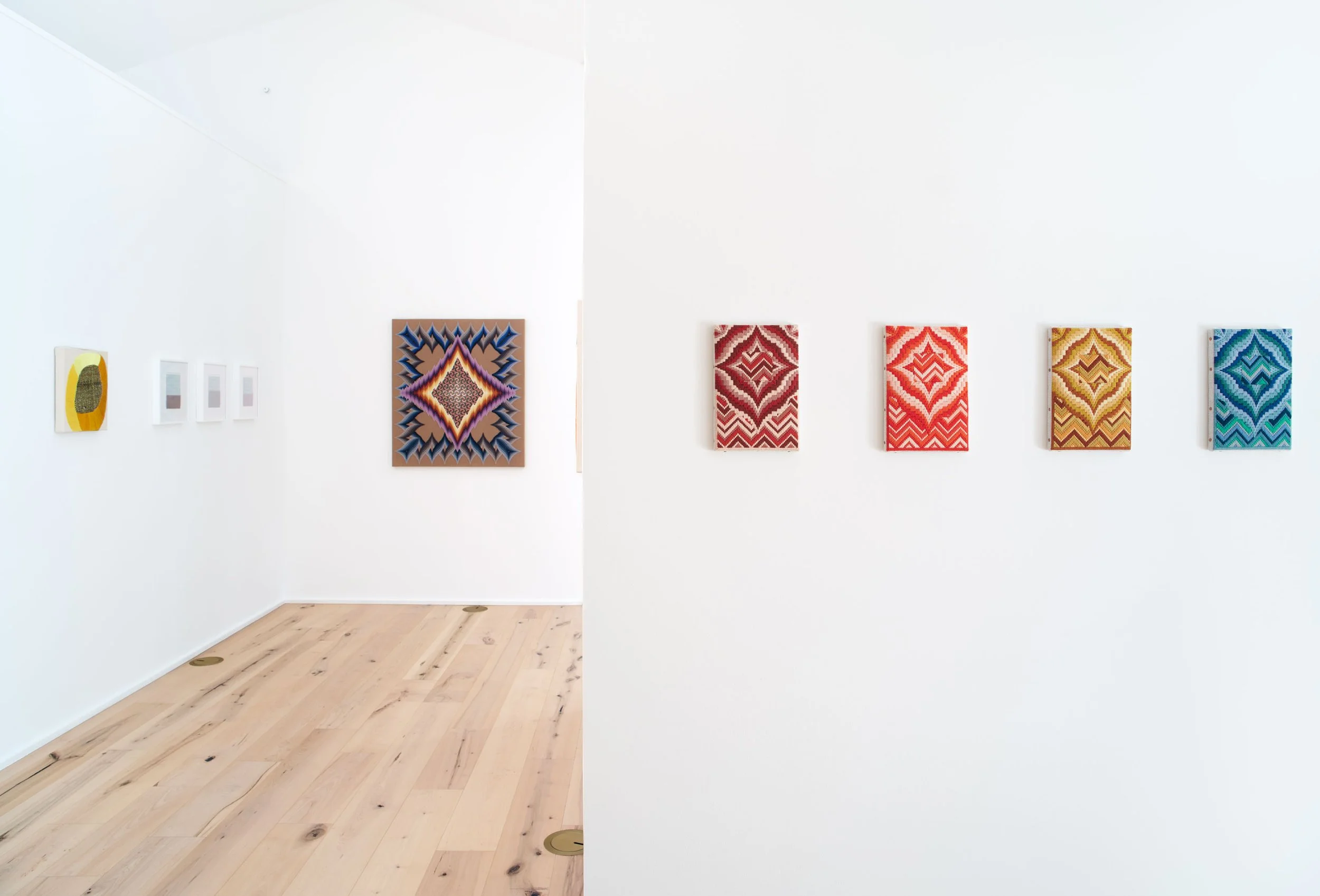 Art gallery featuring colorful woven textile artworks displayed on white walls.