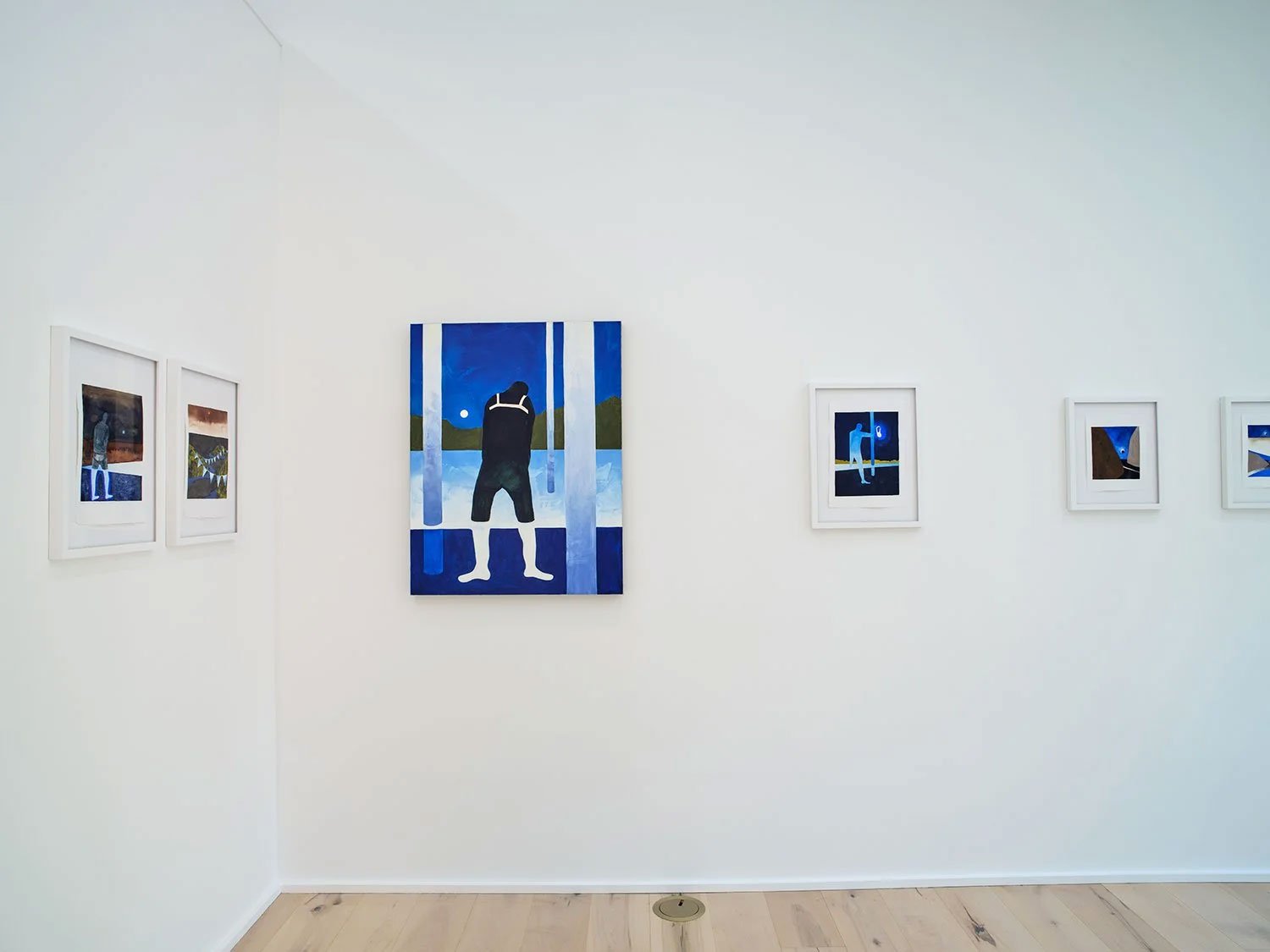 Art gallery wall featuring several framed paintings, including one large blue and black artwork depicting a person looking at a lake scene at sunset or sunrise.