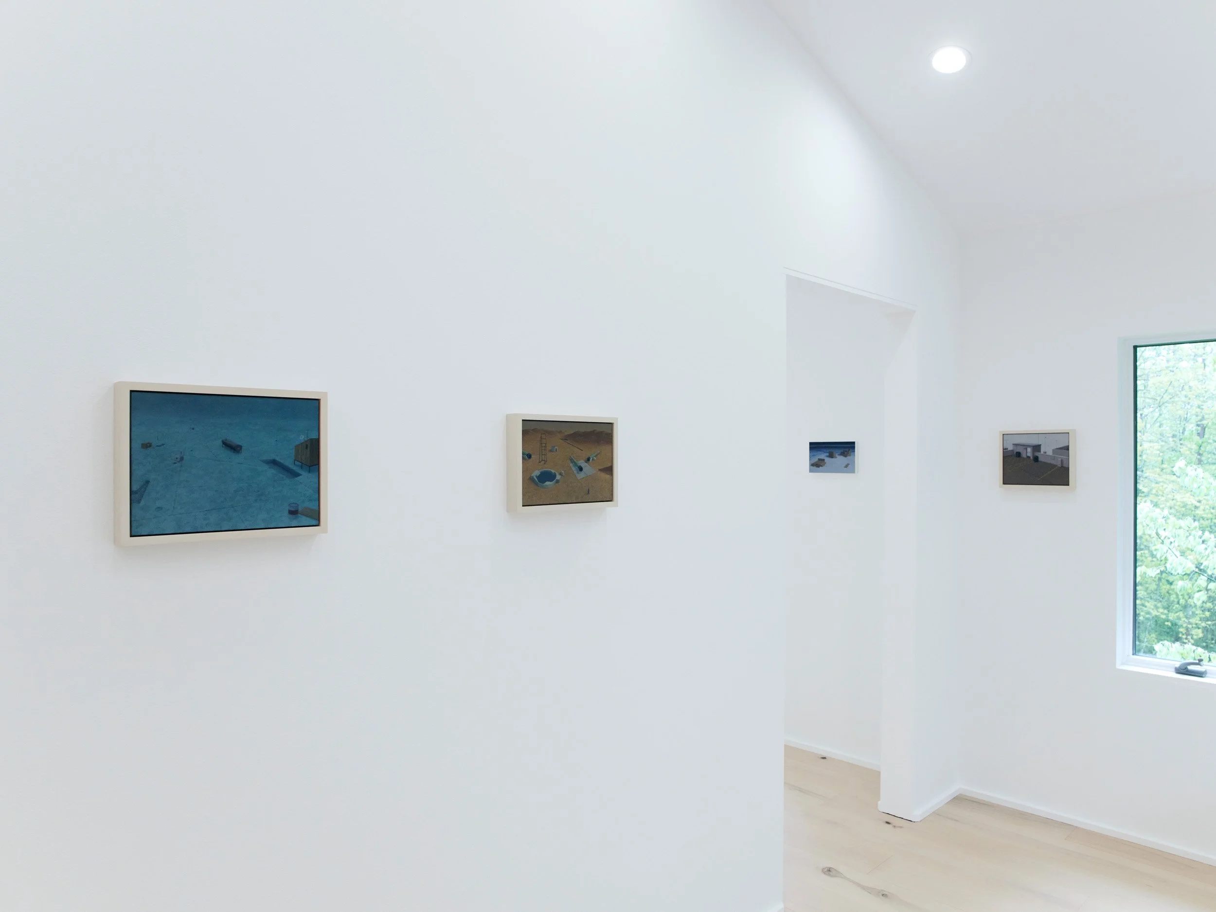 White gallery wall with several framed artworks, a window showing greenery outside, and hardwood floors.