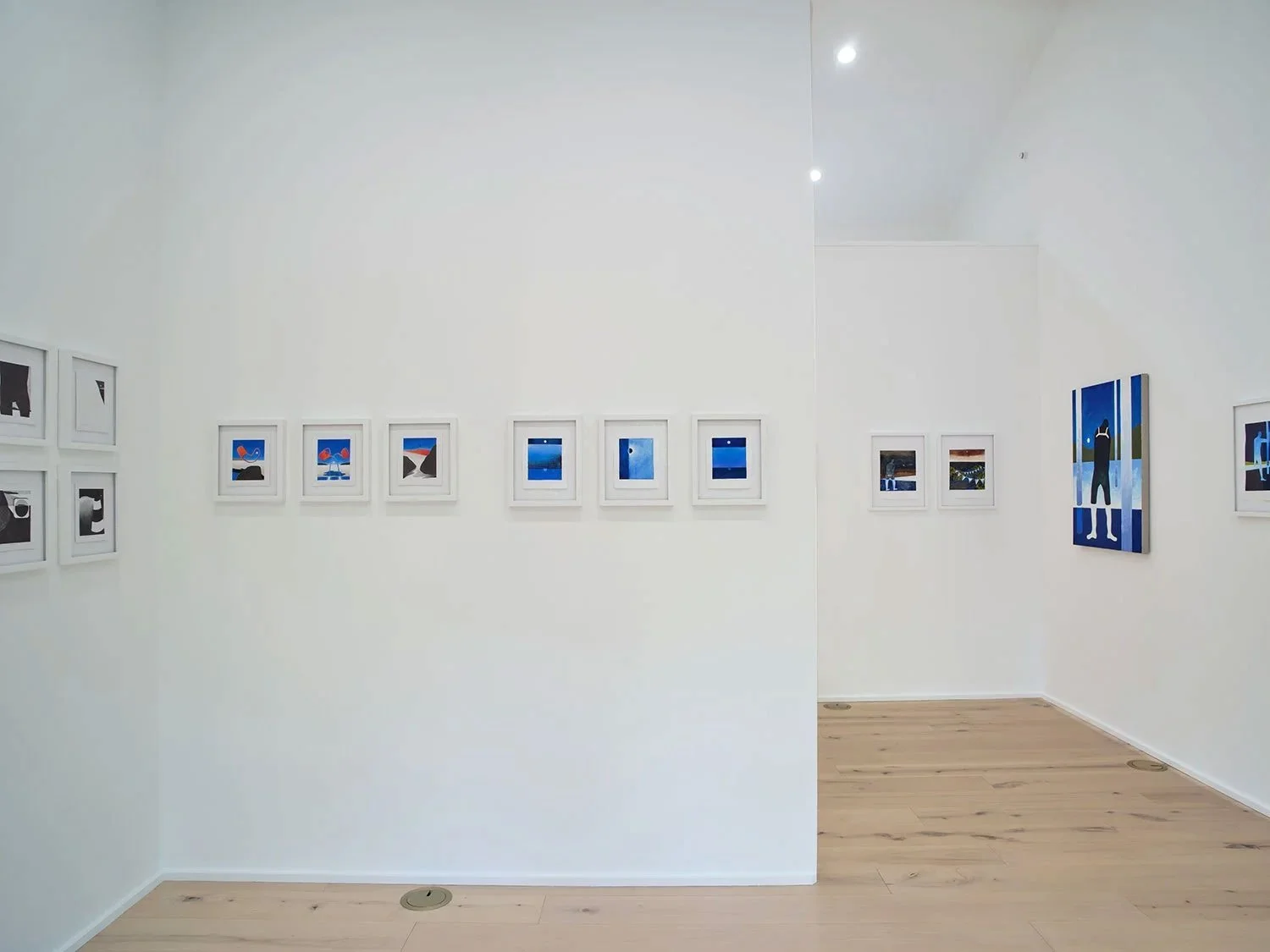 Art gallery with framed photos on white walls, light wood flooring, and ceiling lights.