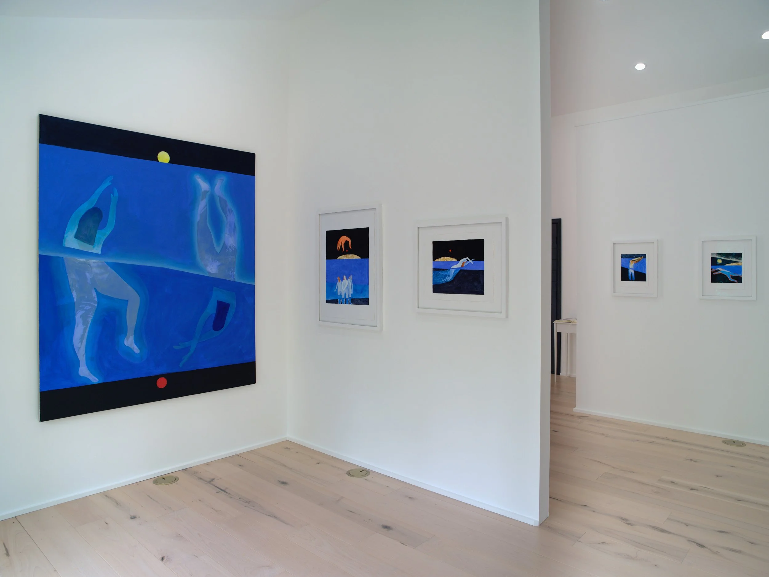 Gallery with abstract blue paintings of human figures and scenes, displayed on white walls with light-colored hardwood floors.