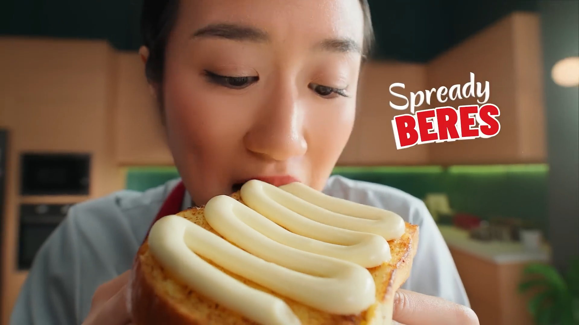 A woman is about to eat a slice of cake with white icing in a kitchen setting.