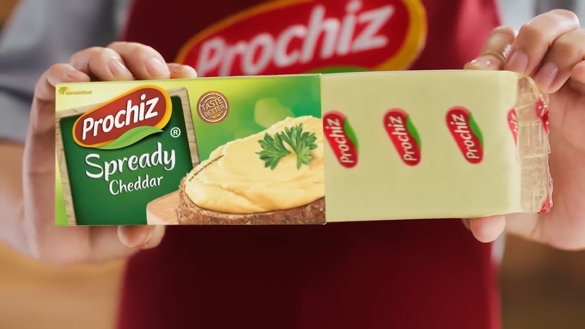 Person holding a box of Prochiz Spready Cheddar cheese, with a close-up view of the packaging featuring an image of cheese spread and parsley on bread.