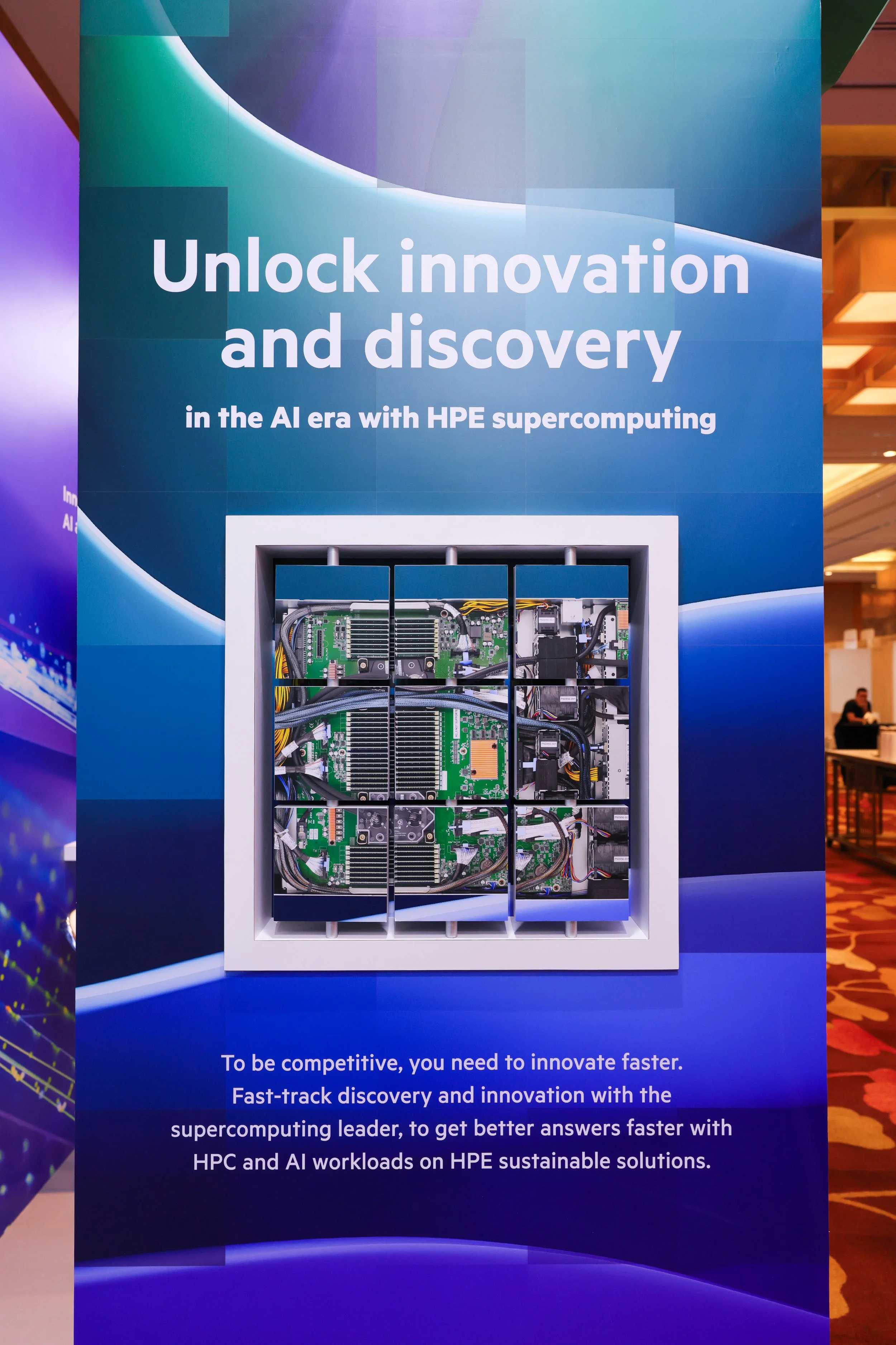 HPE promotional display with text that reads, 'Unlock innovation and discovery in the AI era with HPE supercomputing'. There is a graphic of a computer hardware component behind the text. The background has a gradient of blue and green shades.