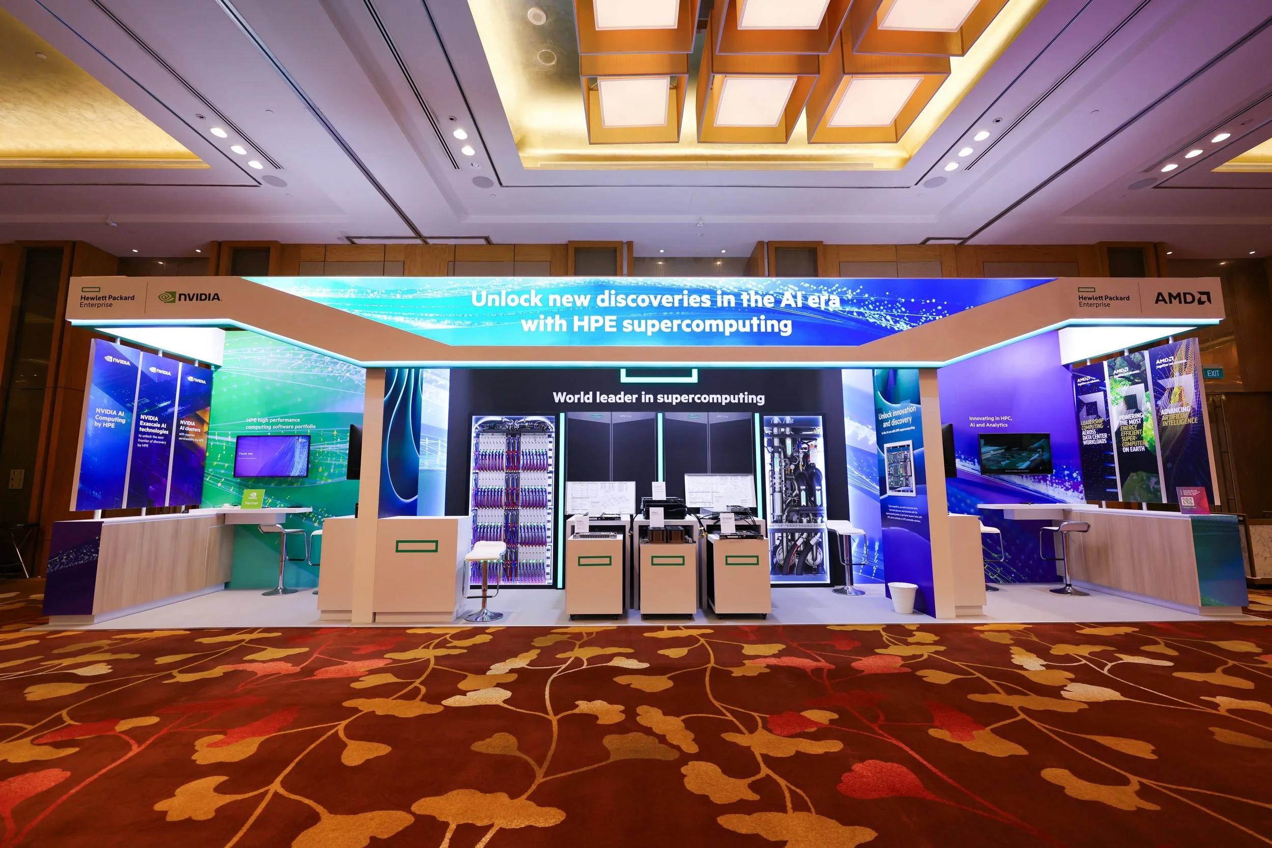 Trade show booth with NVIDIA, AMD, and Hewlett Packard Enterprise branding, displaying computer hardware and information about AI supercomputing, in a conference hall with a floral carpet.