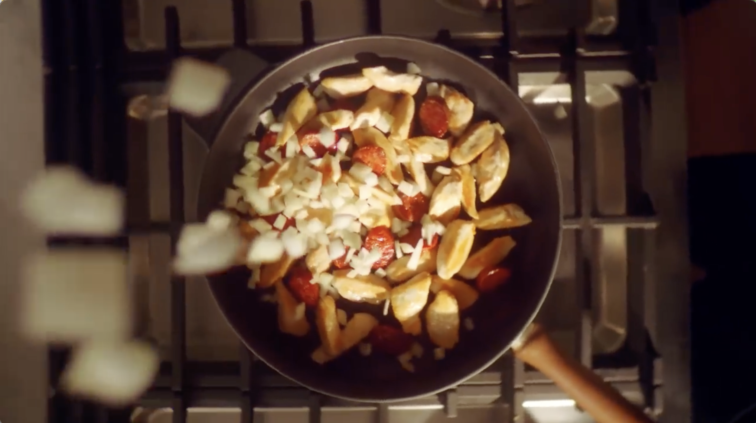 Frying a mix of sliced bananas, strawberries, and chopped onions in a frying pan on a stove.