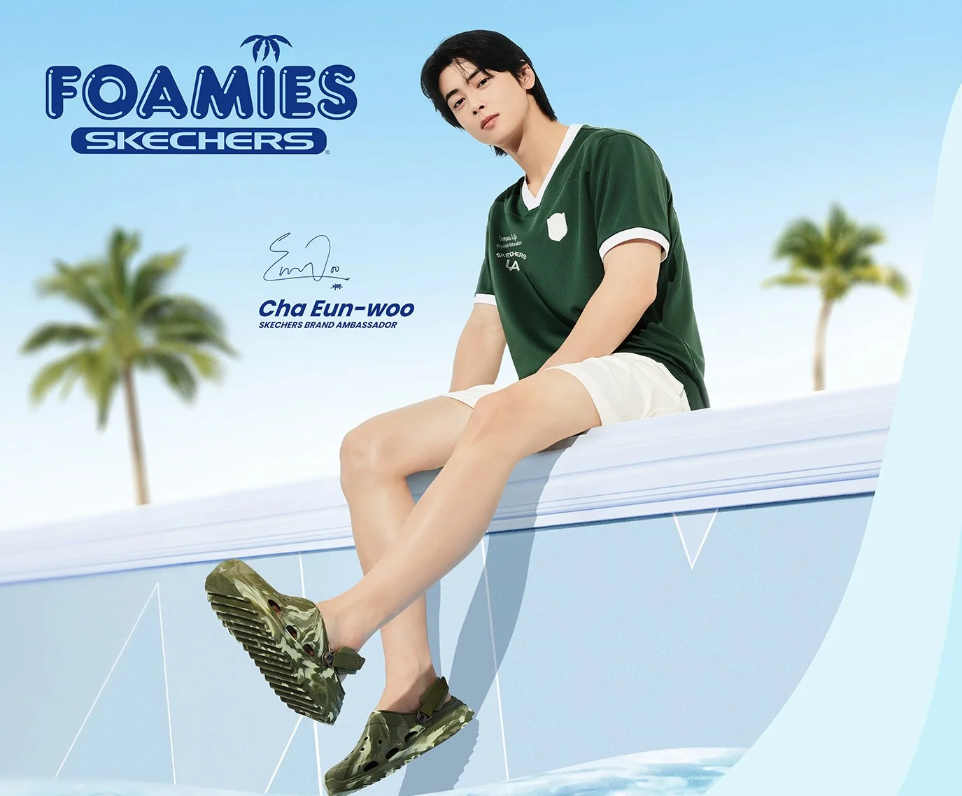 A young man with black hair wearing a green Skechers T-shirt, white shorts, and green Skechers foam shoes, sitting on the edge of a blue pool or structure with palm trees in the background.