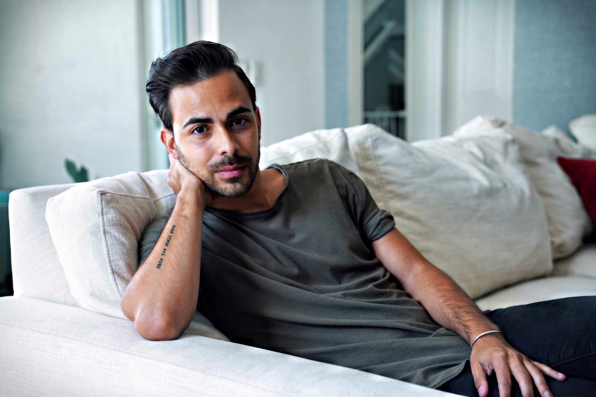 Man sitting on couch resting head on hand: Danny Morales — Gay and Bi Men's Dating Coach reflecting on self-discovery