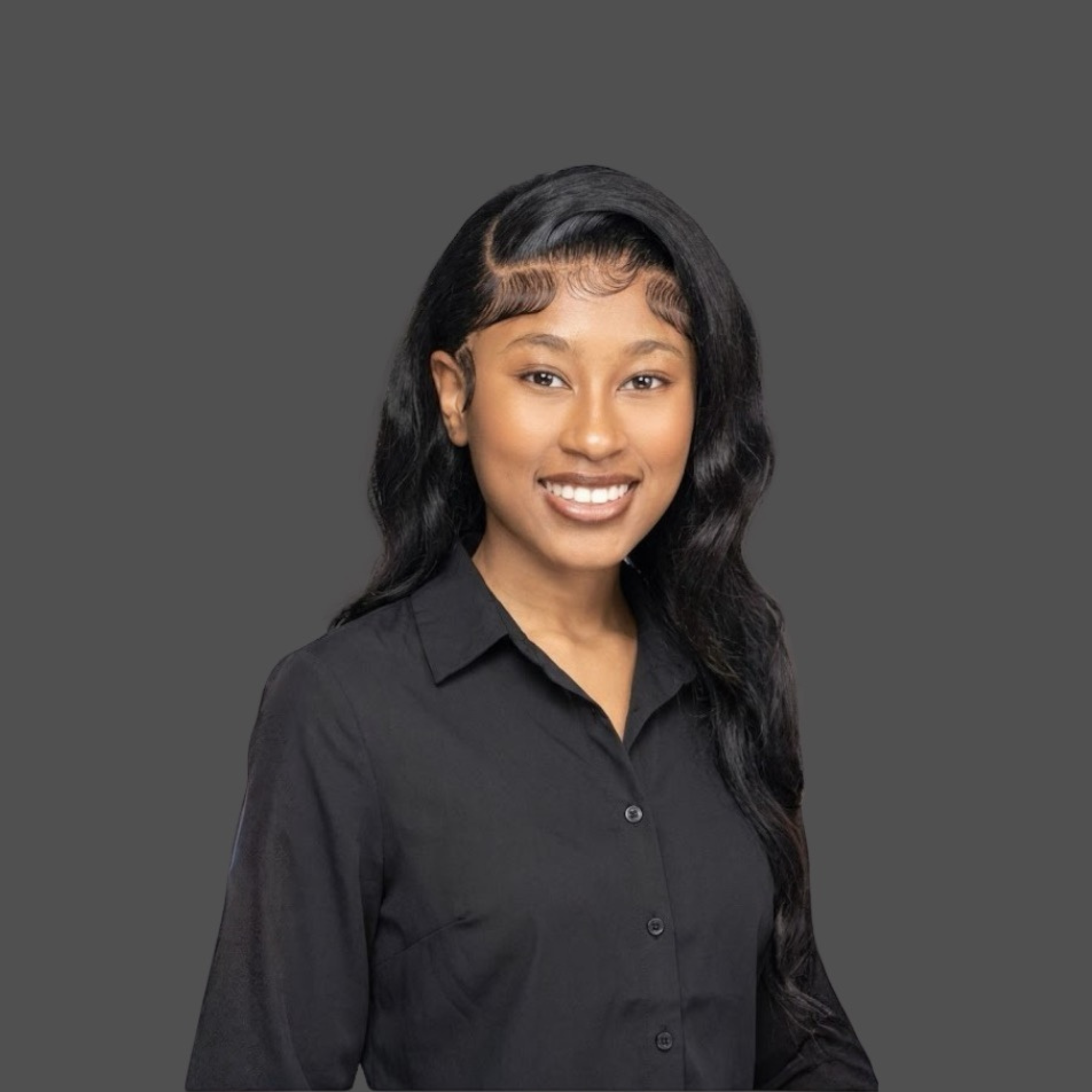 Close up of a woman with long black hair styled in loose waves, wearing a black shirt, smiling against a plain gray background.