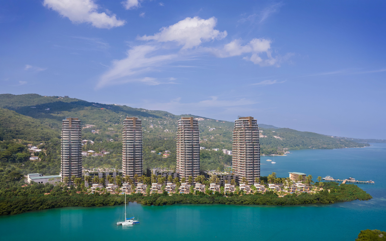 High-rise buildings (The Pinnacle) on a small island surrounded by water, with mountains in the background and a sailboat in the foreground.