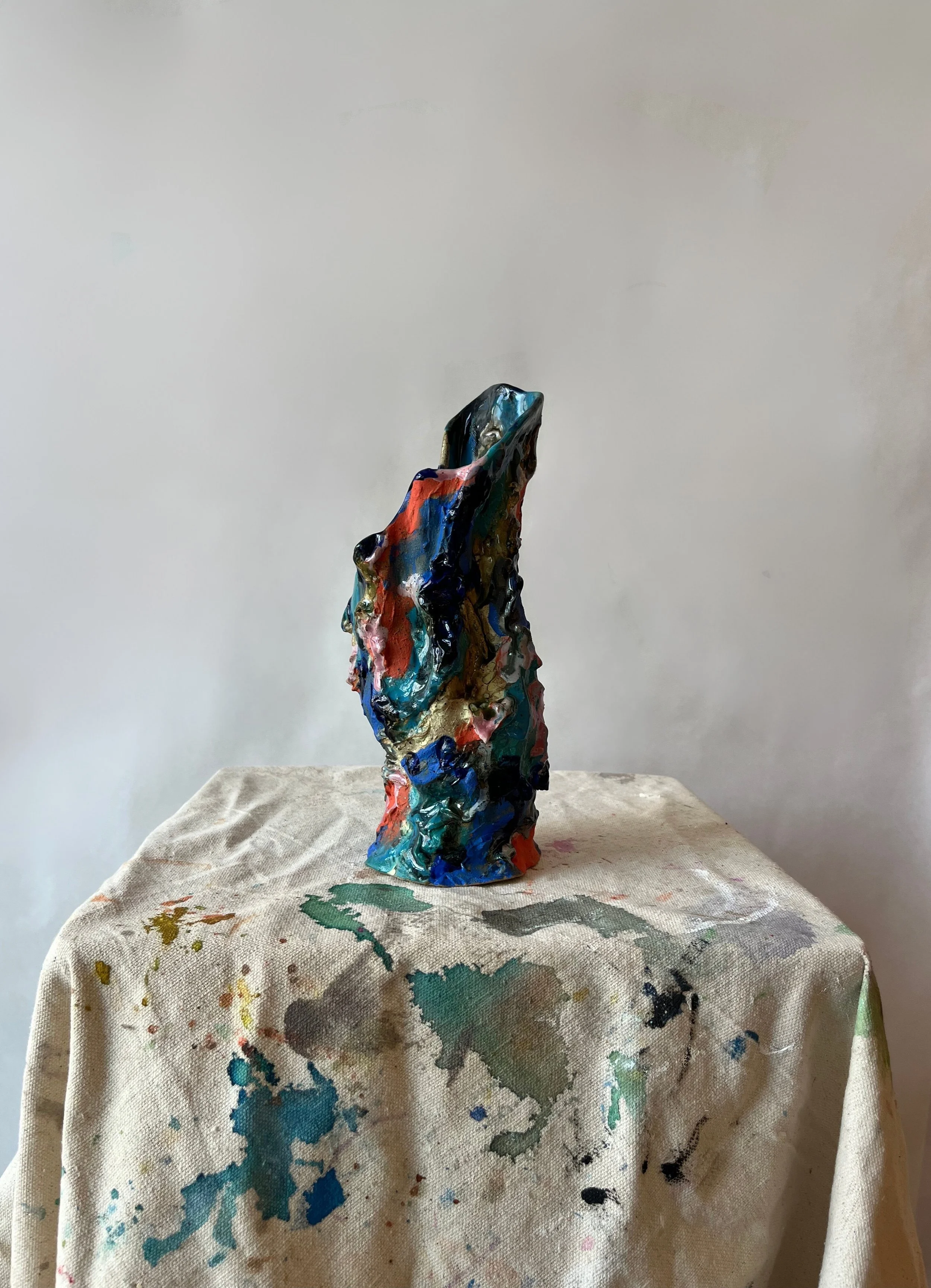 Abstract multicolored sculpture on a paint-splattered cloth-covered table against a plain background.