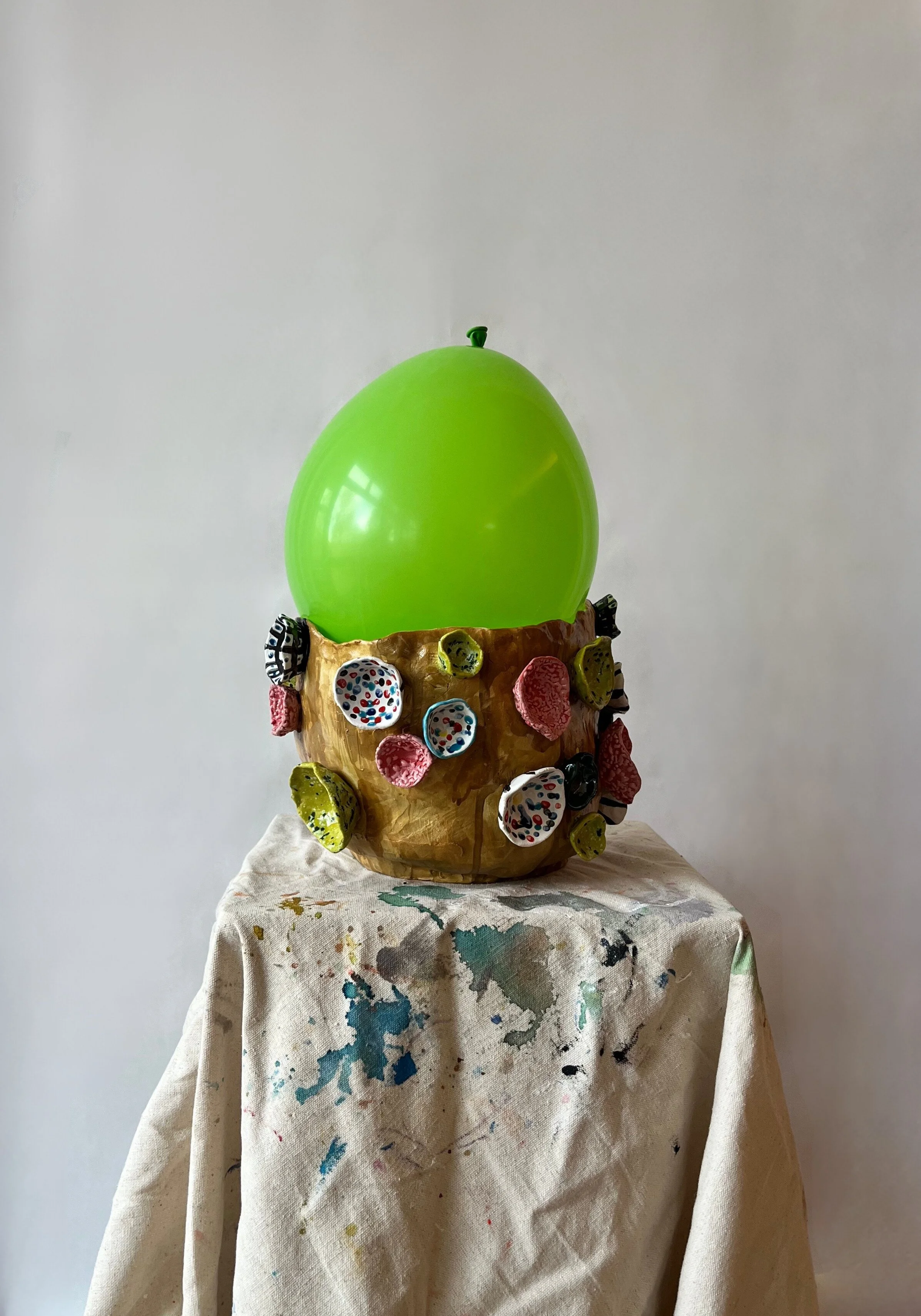 A bowl that looks like a tree trunk with colorful candy-like decorations on the sides, topped with a large, bright green balloon.