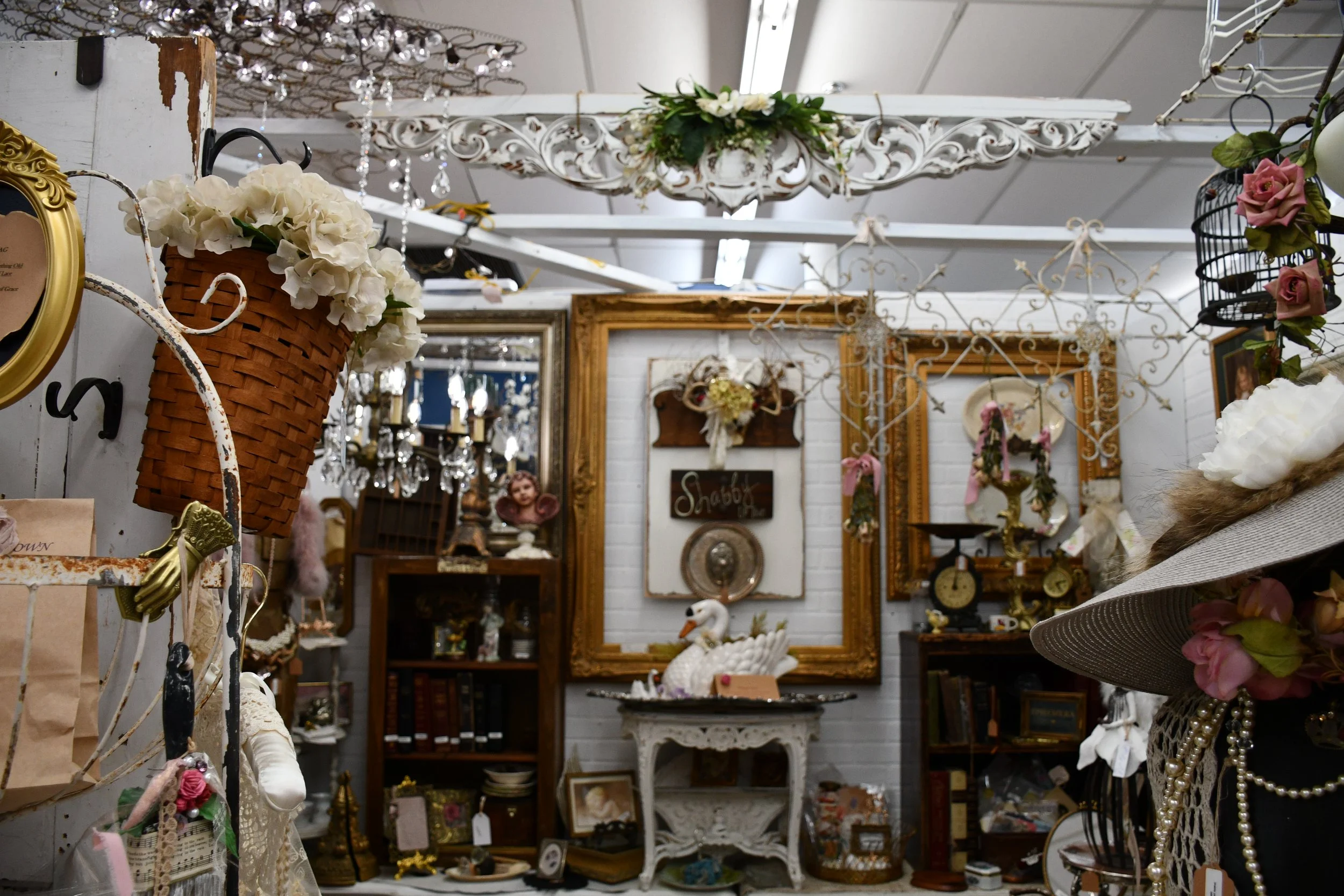An antique shop with vintage decorations and furniture, featuring floral arrangements, framed pictures, and decorative objects.