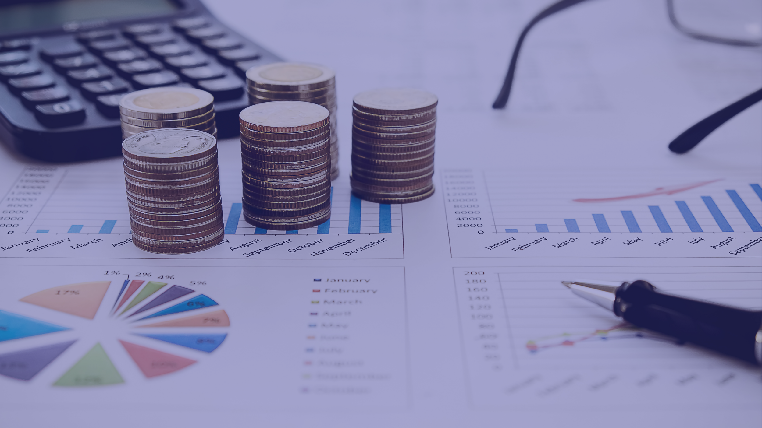 Stacks of coins placed on financial charts, a calculator, eyeglasses, and a pen on a desk.