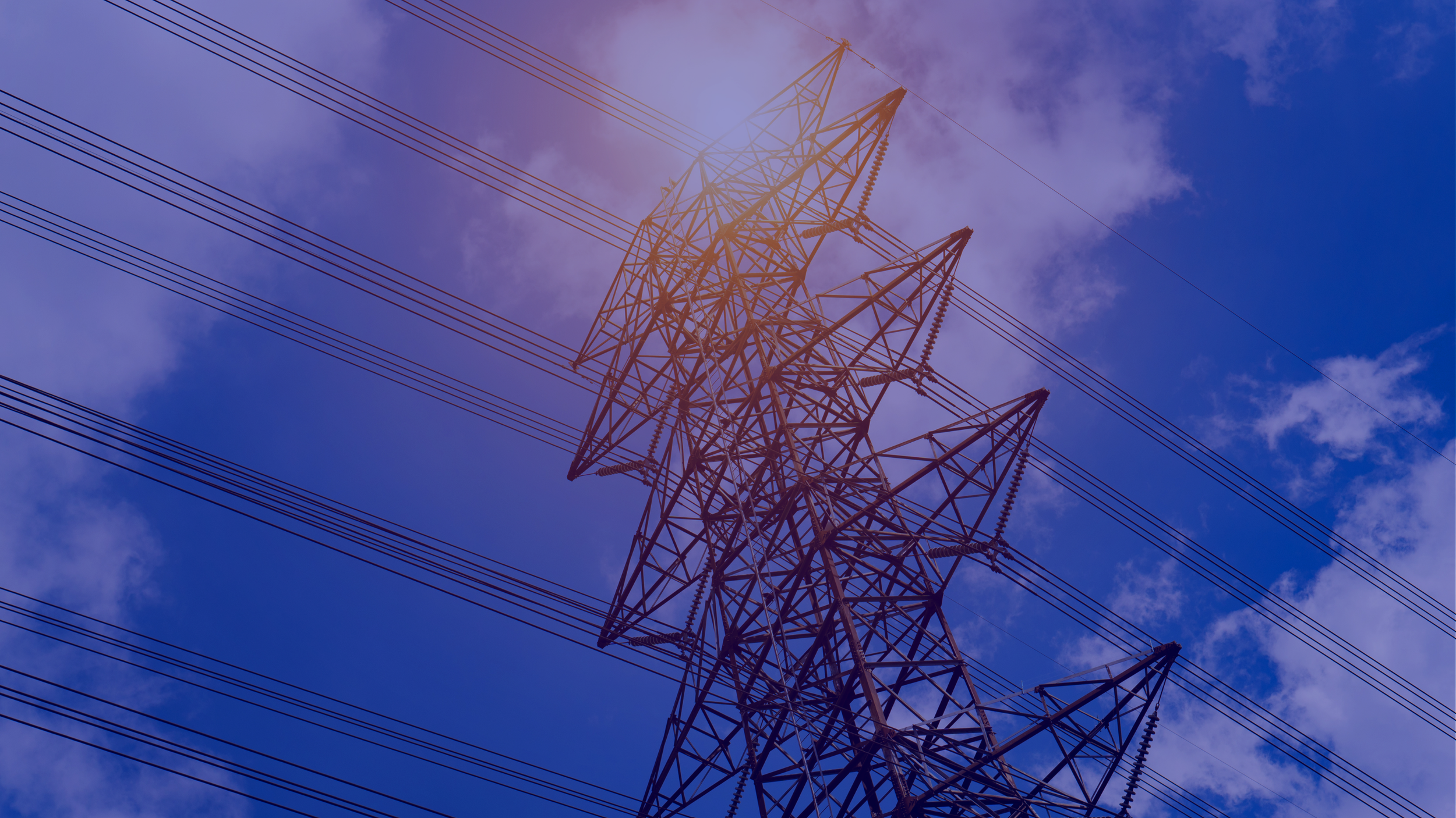 Looking up at a tall lattice steel electrical transmission tower with multiple power lines against a partly cloudy sky.