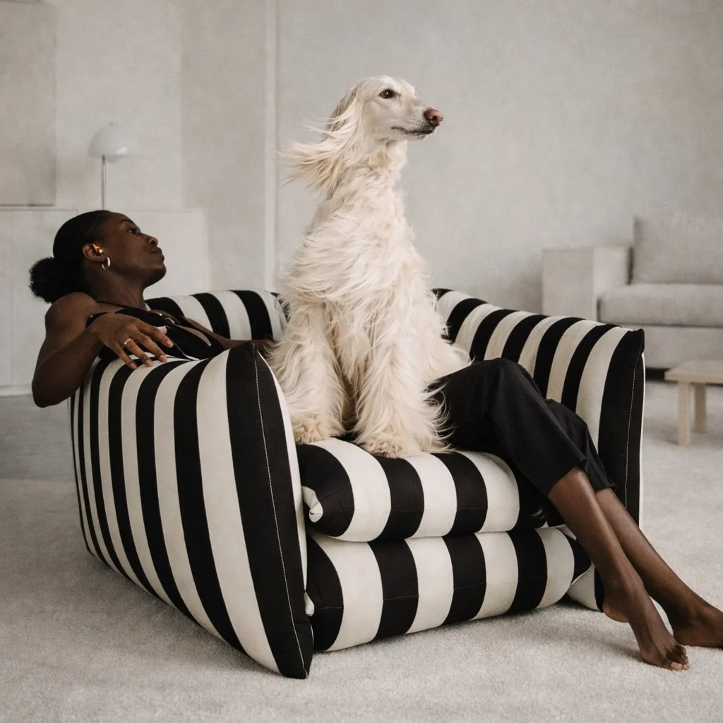 Black woman in modern minimalist interior sitting in black and white striped armchair with fluffy Afghan hound