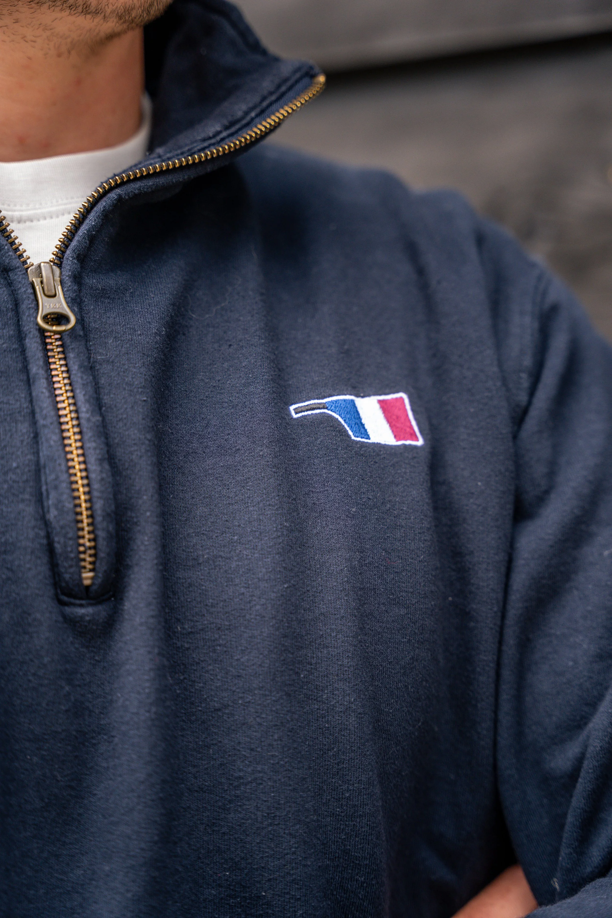 Close-up of a person wearing a navy blue jacket with a small French flag logo on the left chest, in a quarter-zip style, showing part of the person's chin and neck.