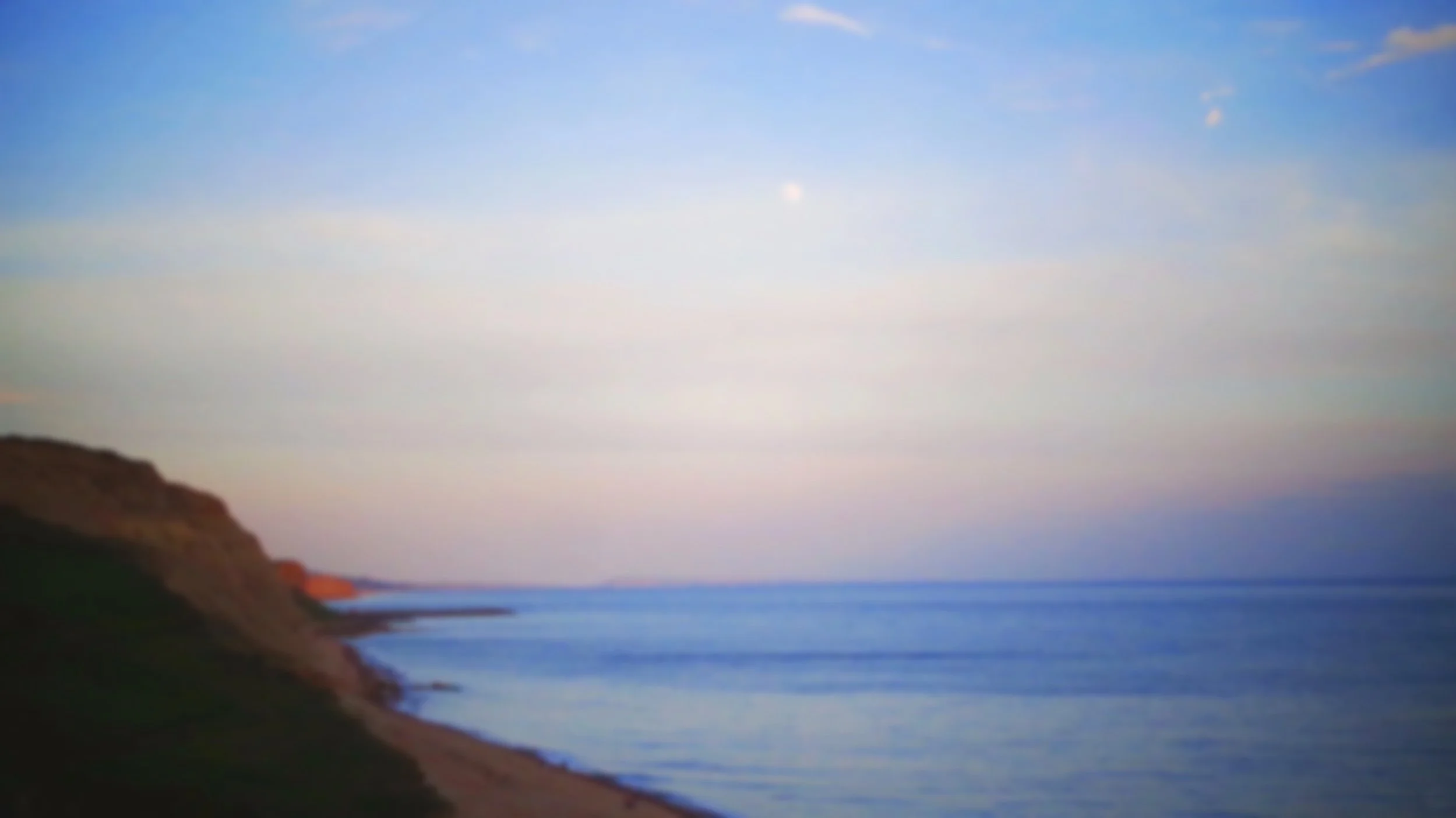 A blurred scenic view of a coastline with cliffs, water, and a cloudy sky.