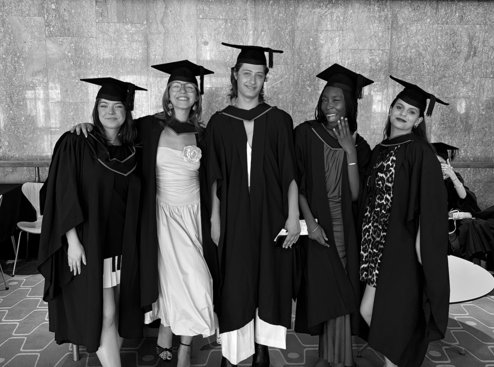 Group of five women in graduation caps and gowns posing together indoors.