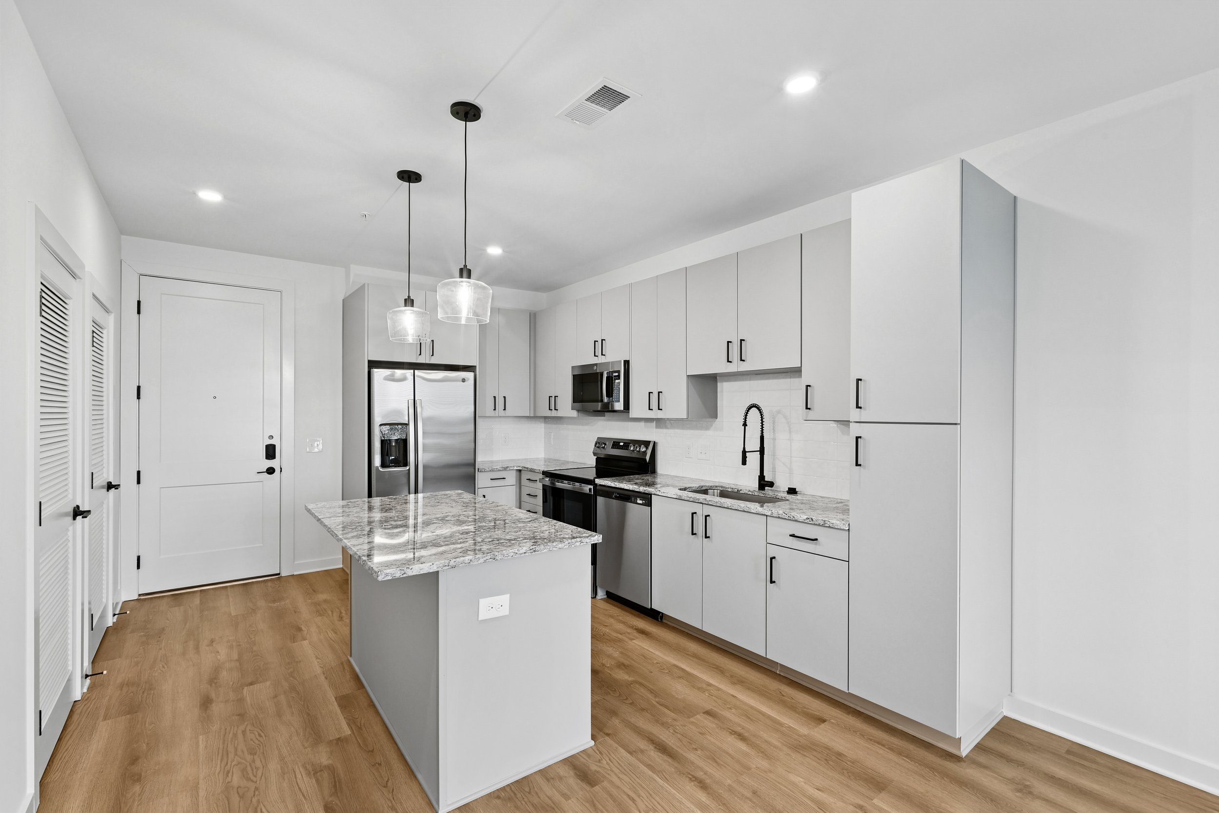 Modern kitchen with white cabinets, stainless steel appliances, granite countertops, and pendant lights hanging above a central island.