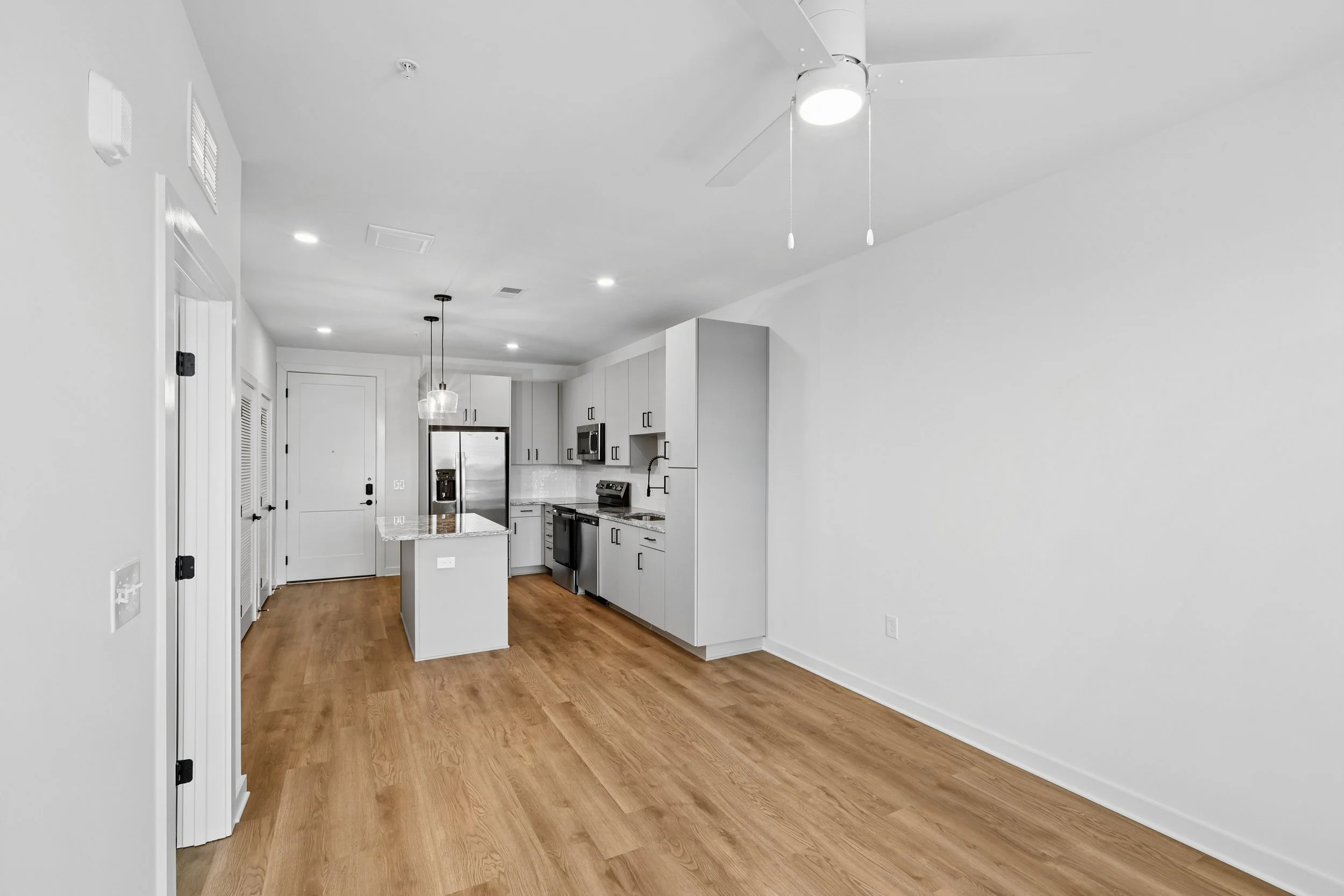 Modern kitchen with white cabinets, stainless steel appliances, hardwood flooring, and a white ceiling with recessed lighting and ceiling fan.