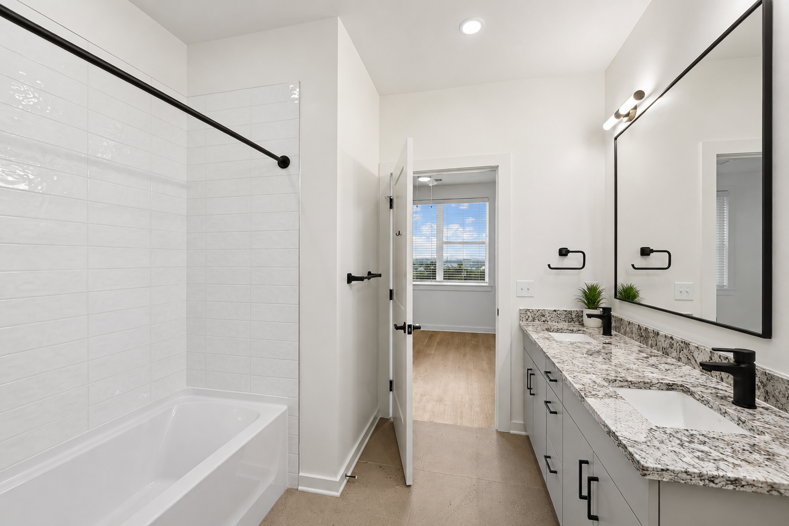 Modern bathroom with white walls, black fixtures, a granite countertop with dual sinks, a large mirror, a bathtub, and a window with blinds showing a blue sky with clouds.