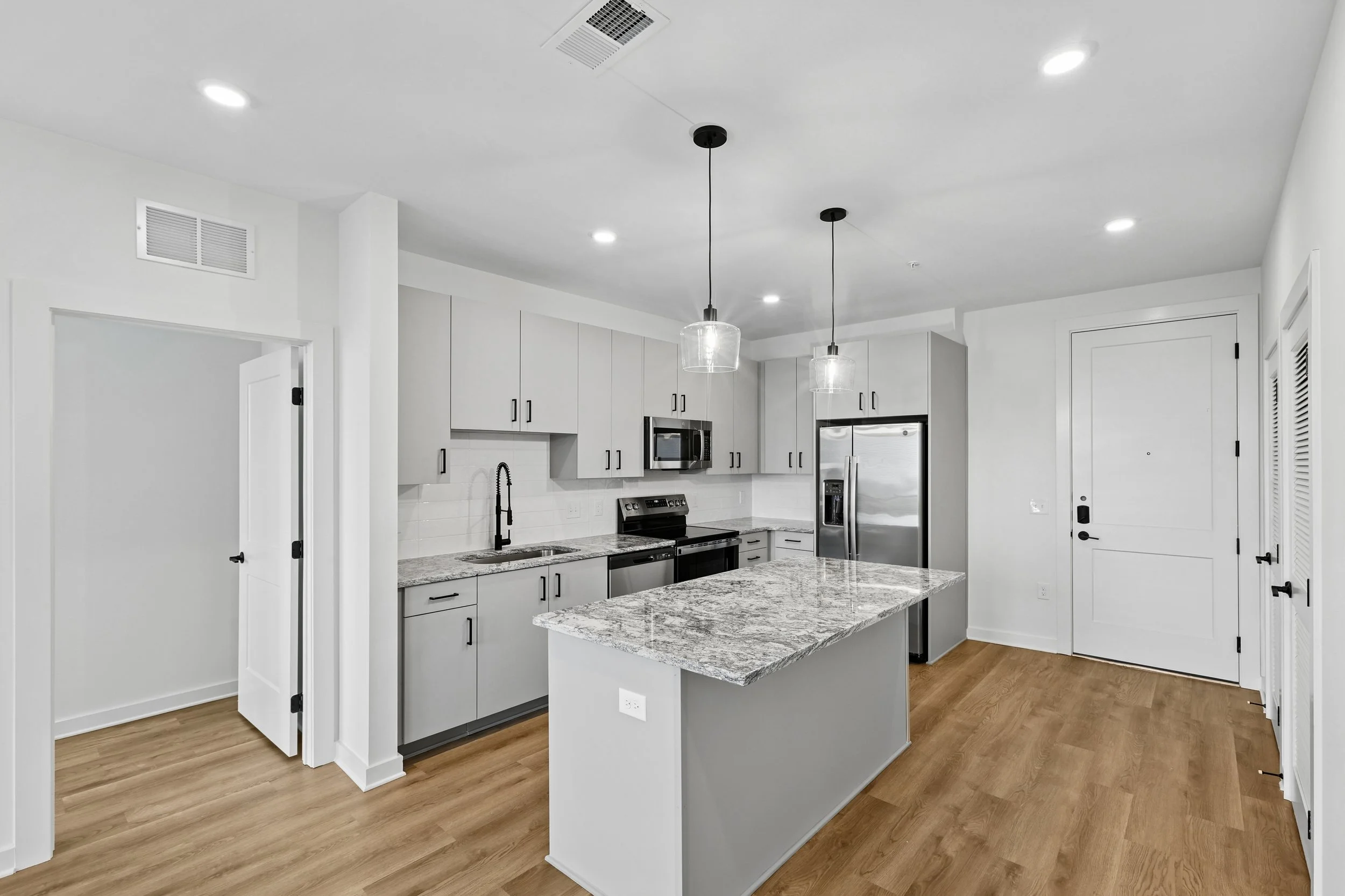 Modern kitchen with white cabinets, gray granite countertops, stainless steel appliances, and pendant lights over an island