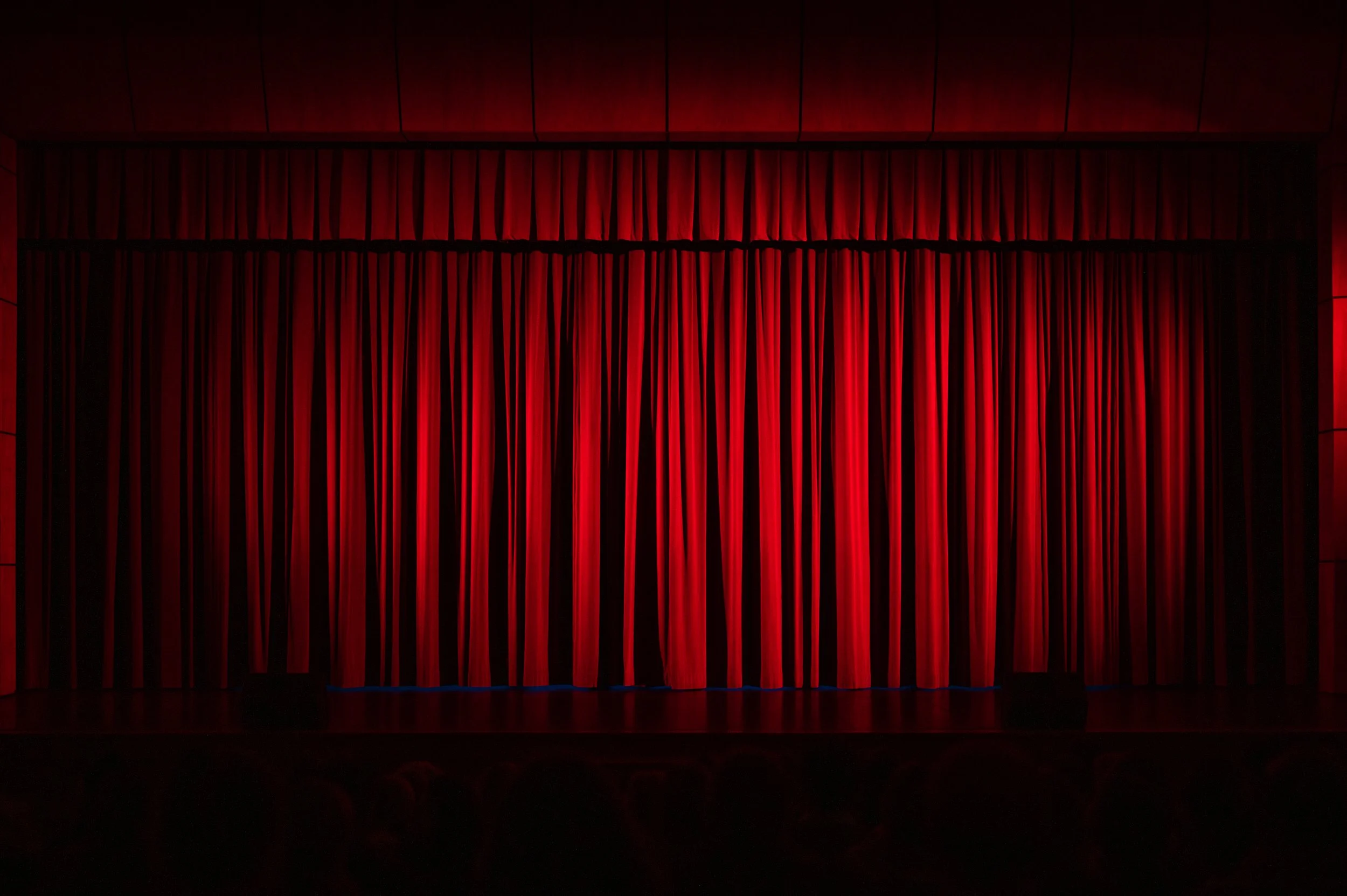 Closed red theater curtain hanging on stage with wooden walls.