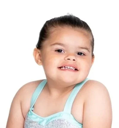 Child with a mischievous smile, wearing a light blue tank top, against a white background.