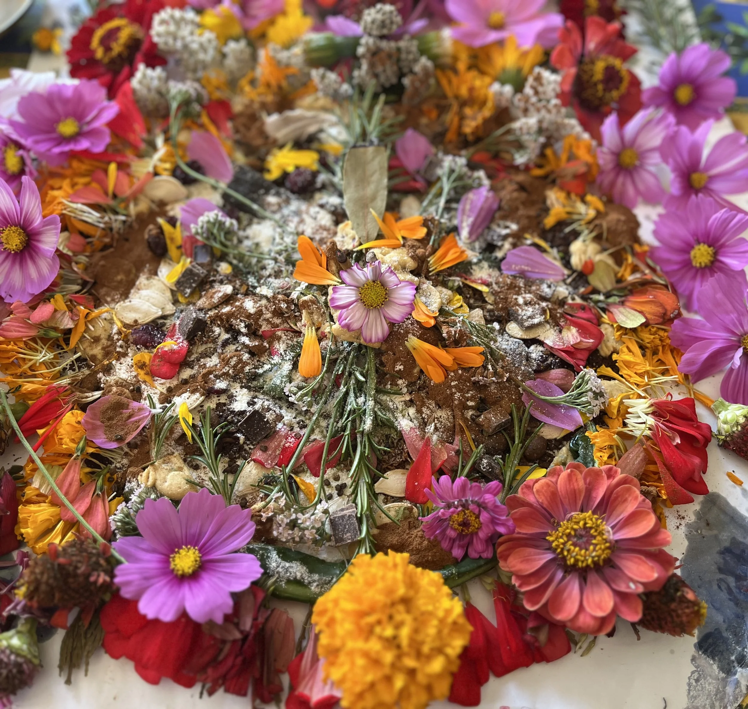 Colorful flower petal offerings arranged on the ground, featuring pink, red, orange, yellow, and white petals, with some leaves and powdered substances.