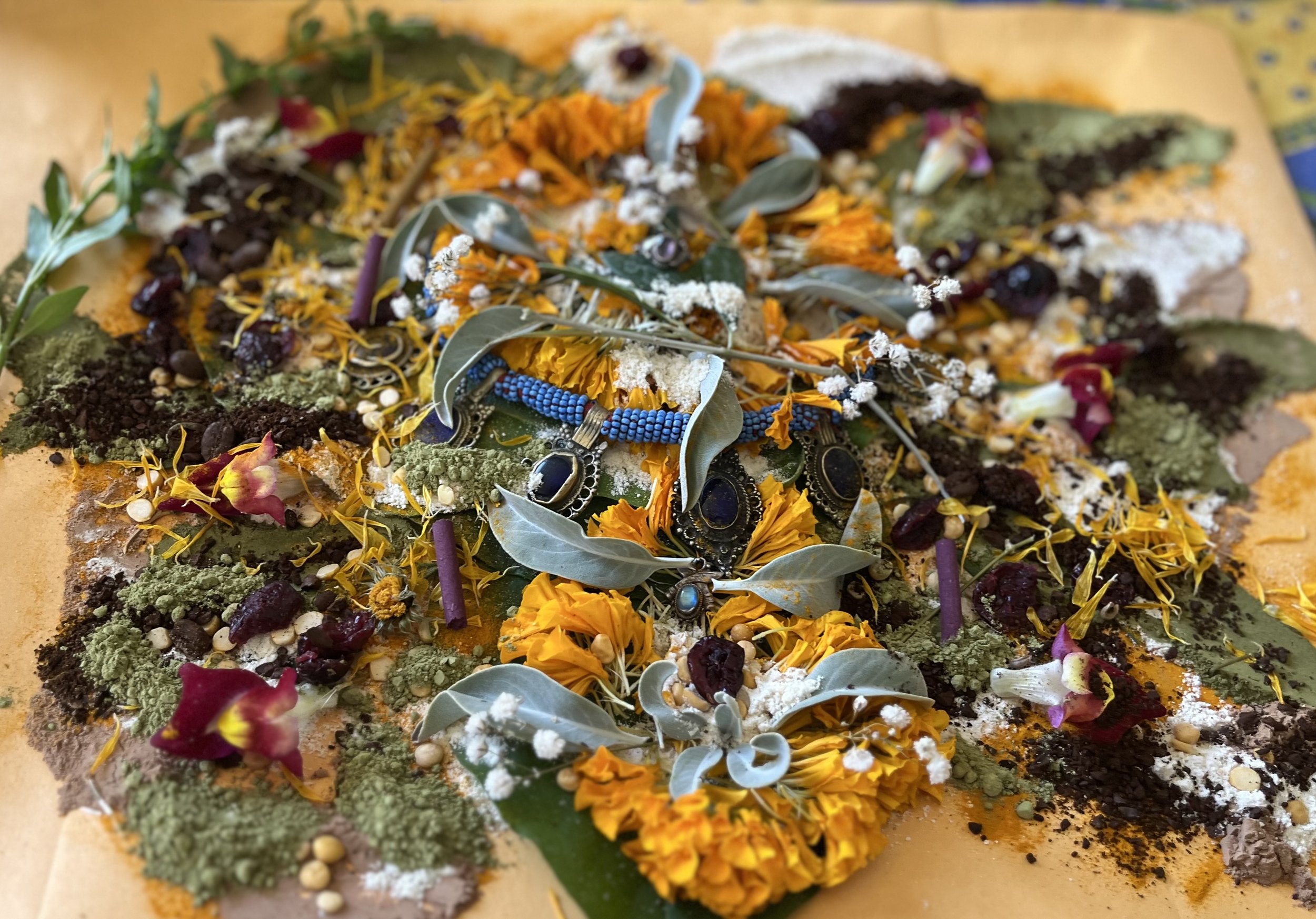 Close-up of a colorful floral and herbal arrangement with various leaves, flowers, and natural elements laid out on a surface.