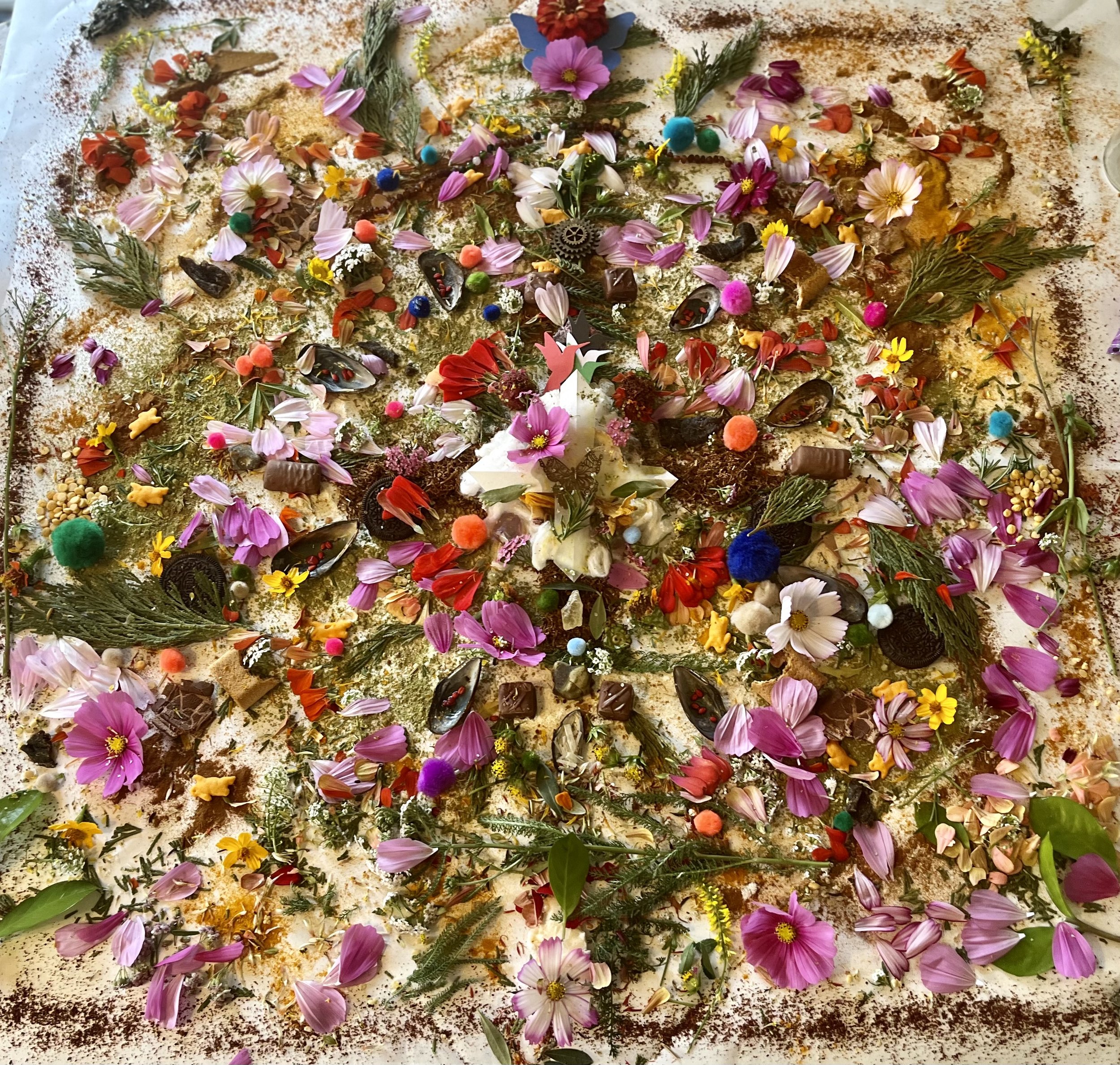 A large collection of colorful flowers, leaves, and small decorative items spread out on a surface, likely for decoration or a ritual.