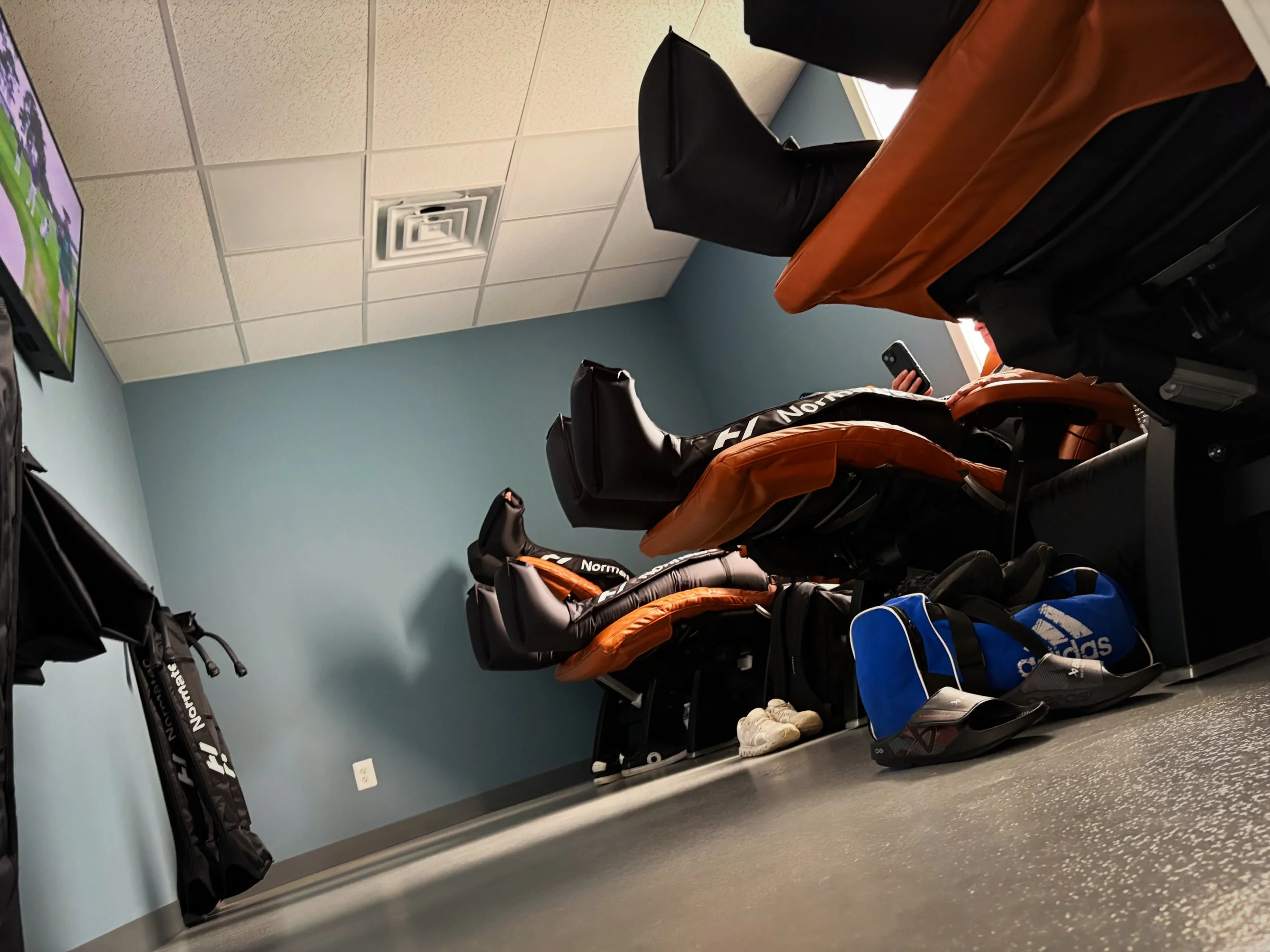 A room at Elite Edge Recovery in Malvern, PA filled with people sitting in zero-gravity chairs doing compression therapy.