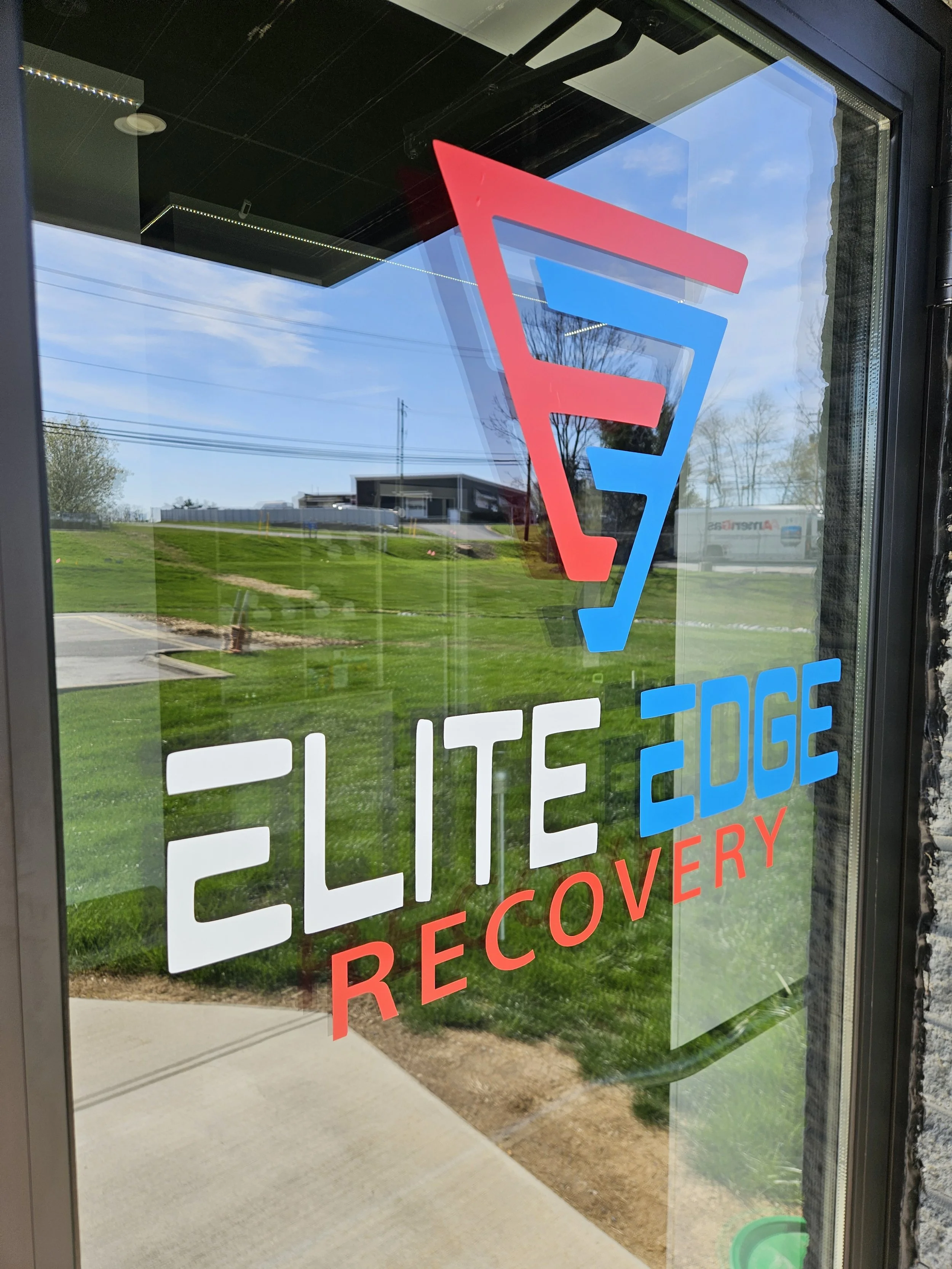Window decal with the logo of Elite Edge Recovery, featuring a stylized 'E' in red and blue, along with the company name in white and blue letters and the word 'Recovery' in red.